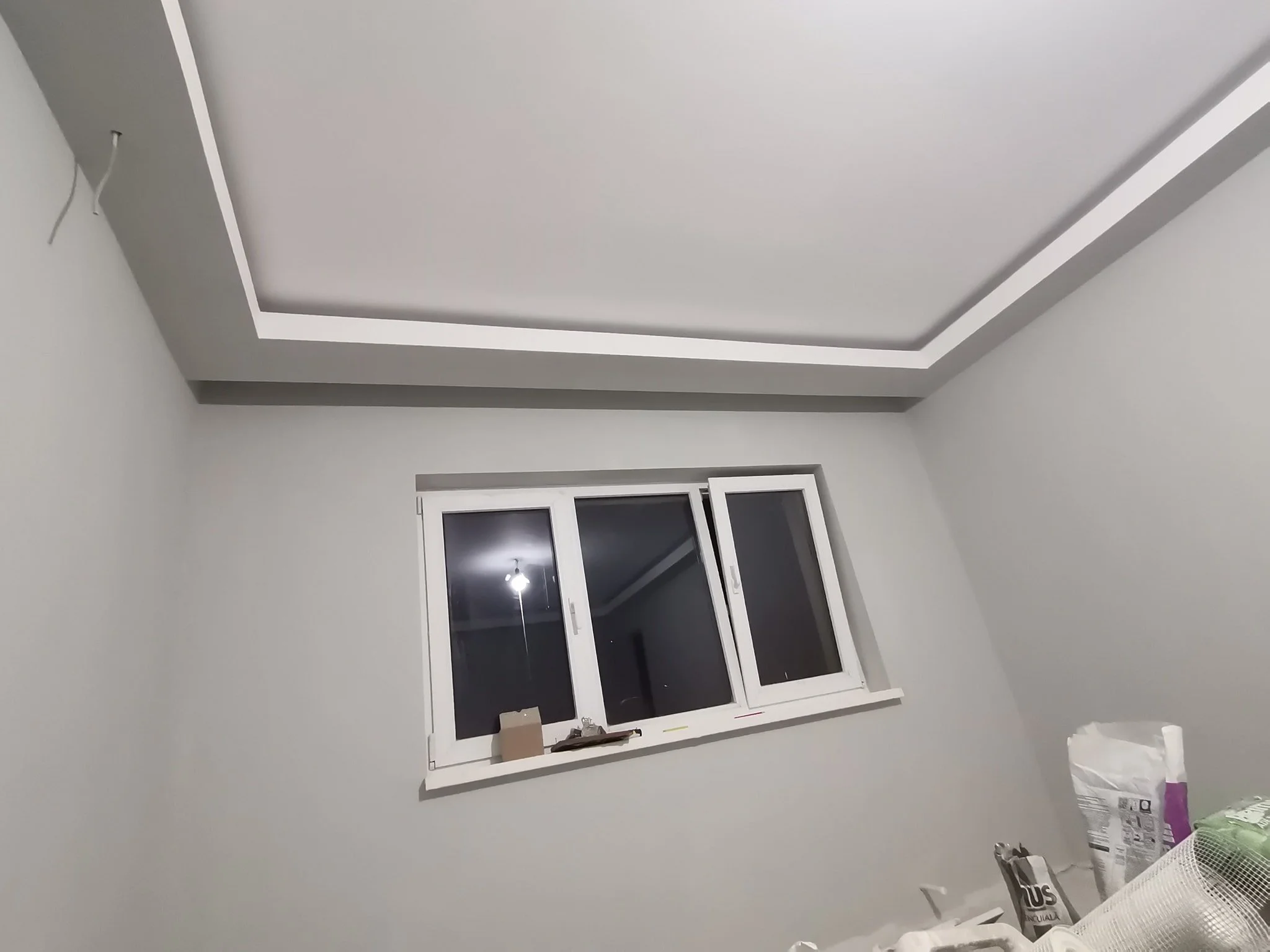 Room under construction with a white window, gray walls, and construction materials on the floor.