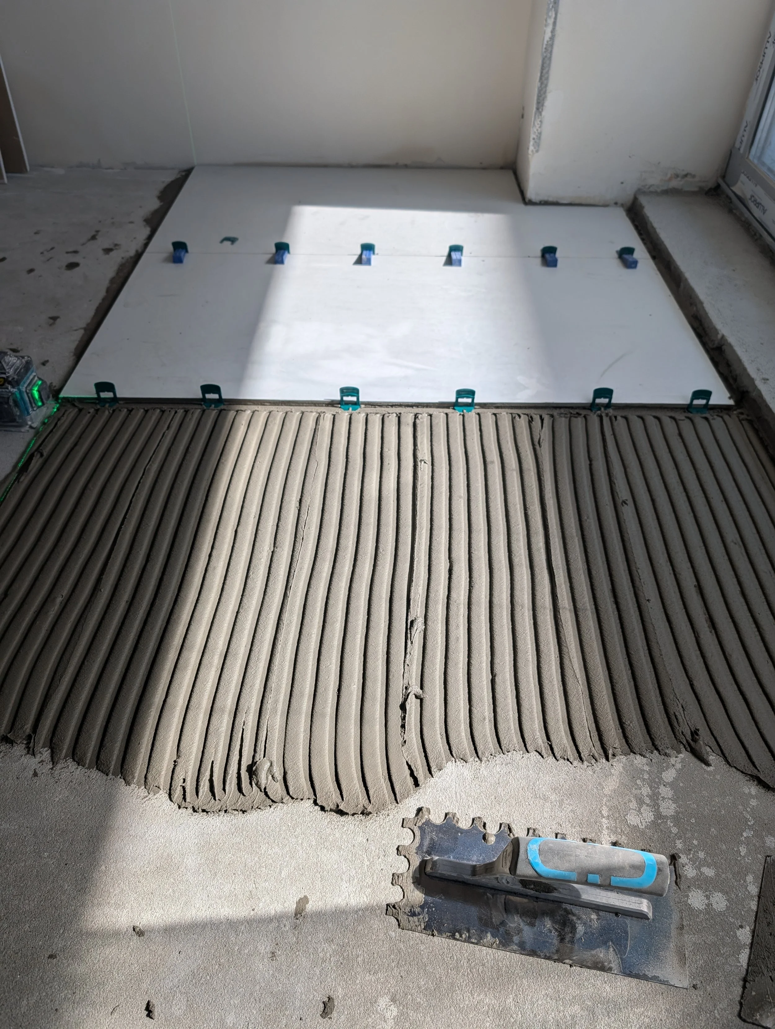 Construction site with a partially installed shower or flooring system, with a large white sheet secured by clips and a tile saw on a concrete surface.