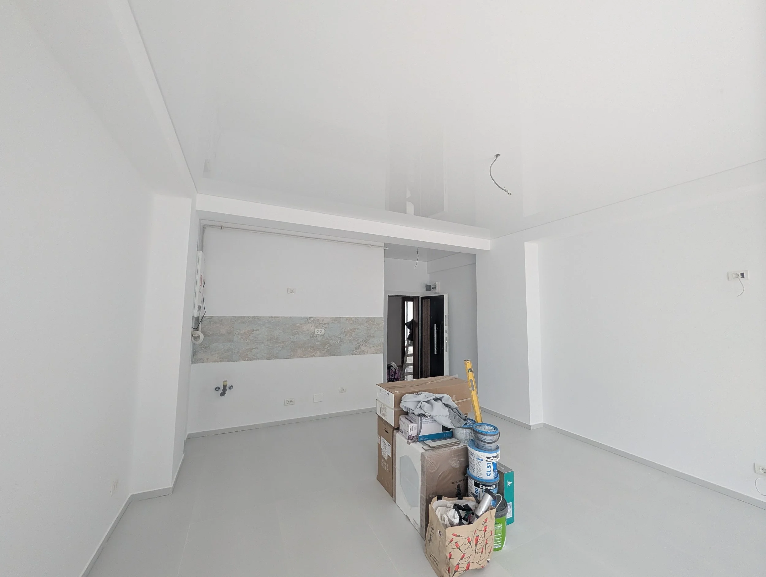 Interior of a room under construction with unfinished white ceiling and walls, boxes, paint cans, and construction tools on the floor.