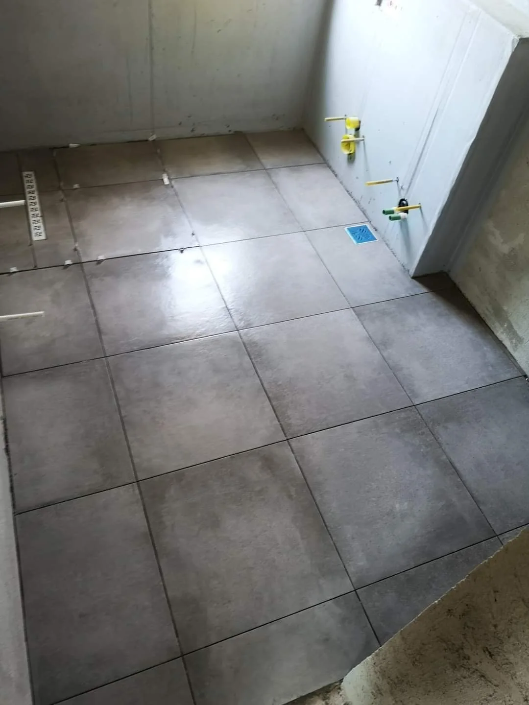 Construction site with tiled floor, plumbing pipes, and a floor drain, unfinished walls.