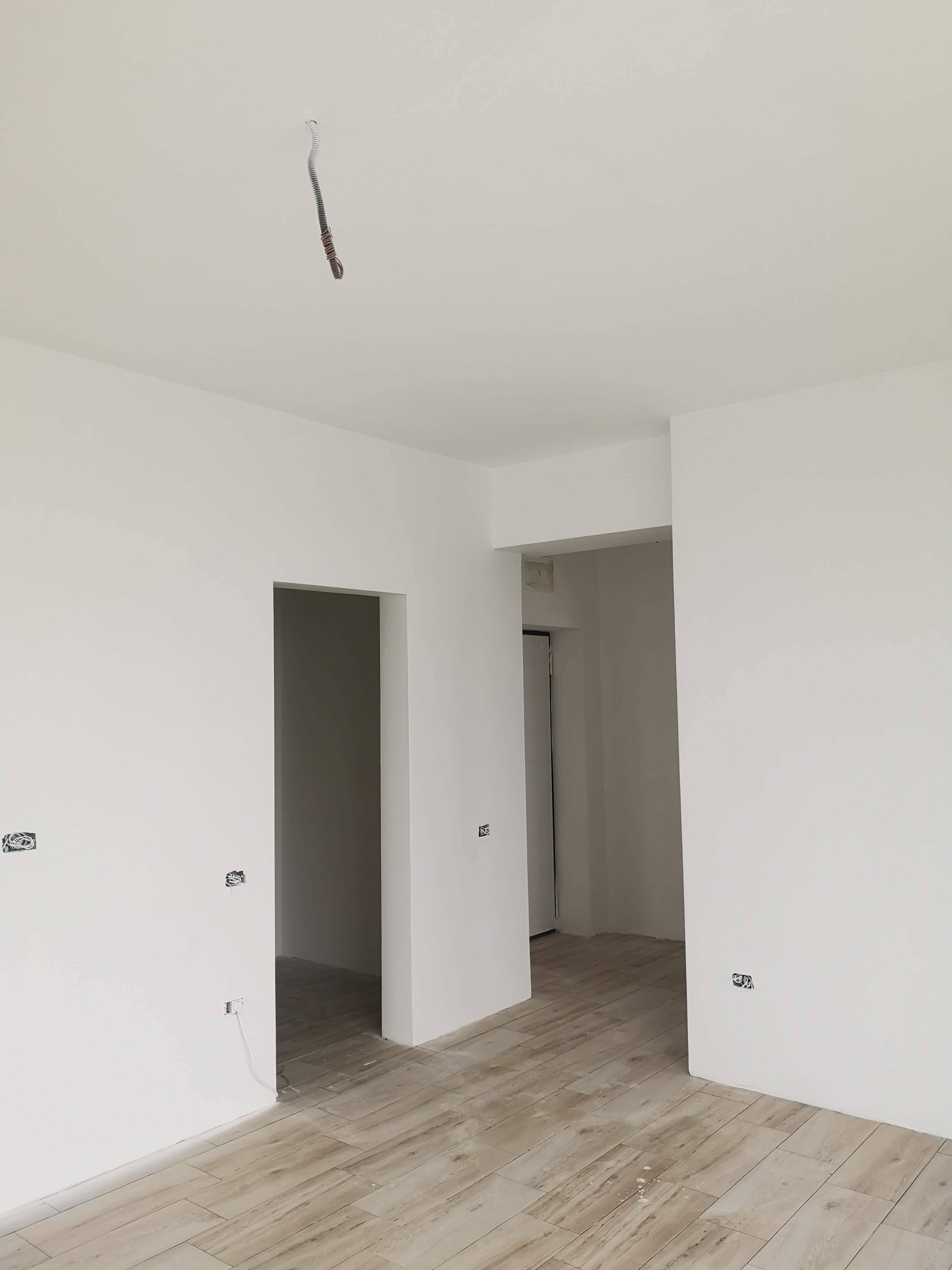 Empty room with white walls, light wood flooring, and unfinished electrical outlets and wiring.