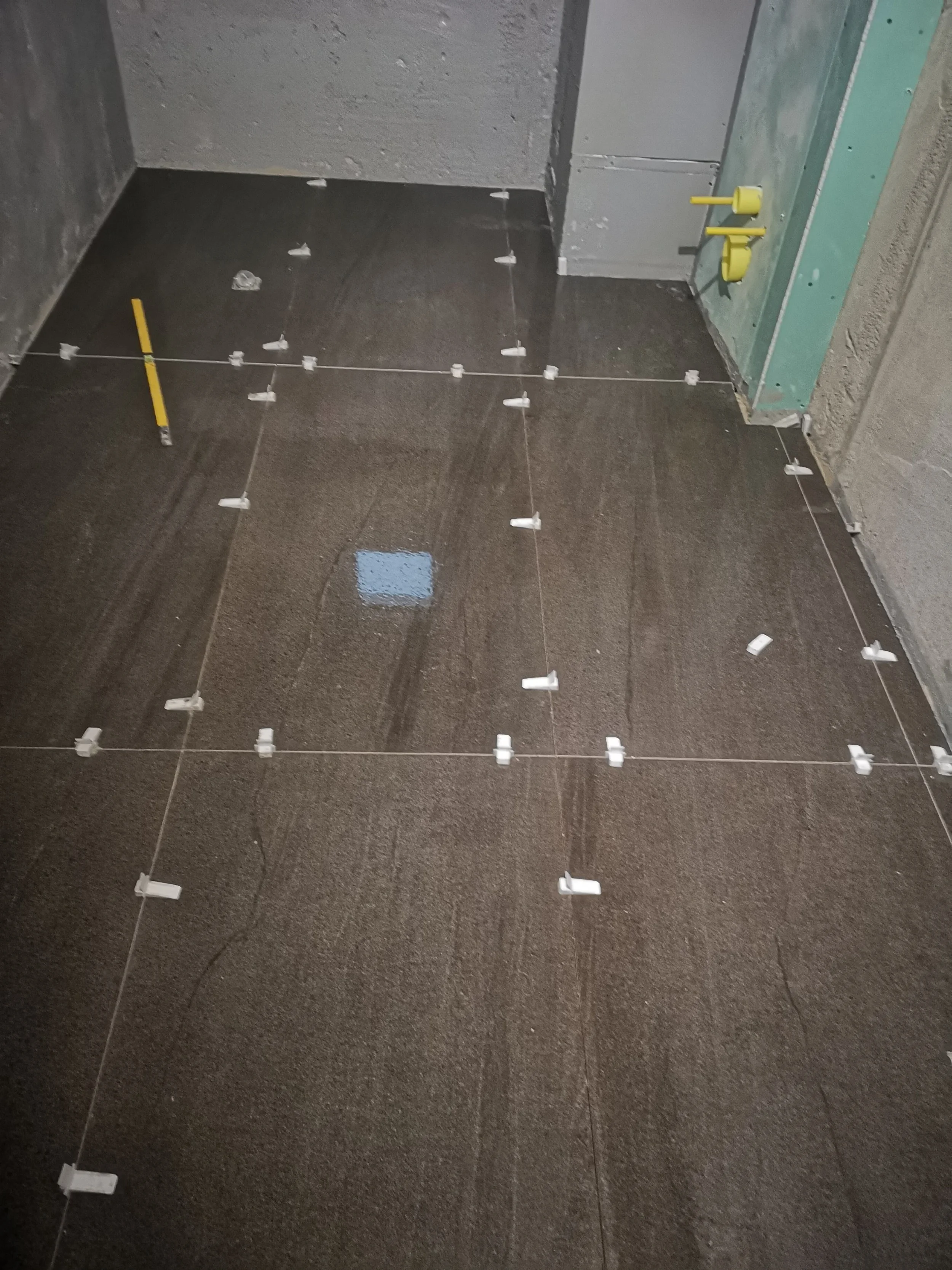 View of a tiled bathroom floor under construction with tile spacers and a level tool in place.