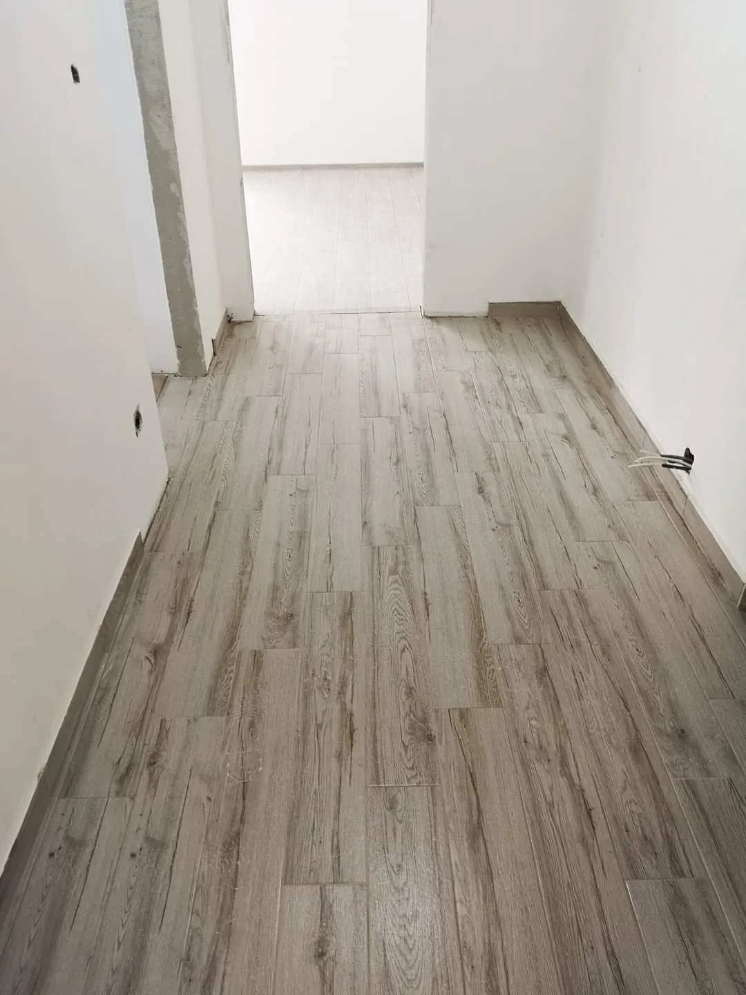 Empty room with light woodgrain flooring and white walls, with a doorway at the end leading to another room.