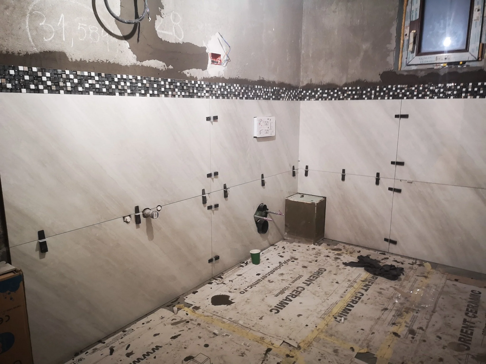 Under construction bathroom with partially tiled wall, plumbing fixtures, and construction materials on the floor.