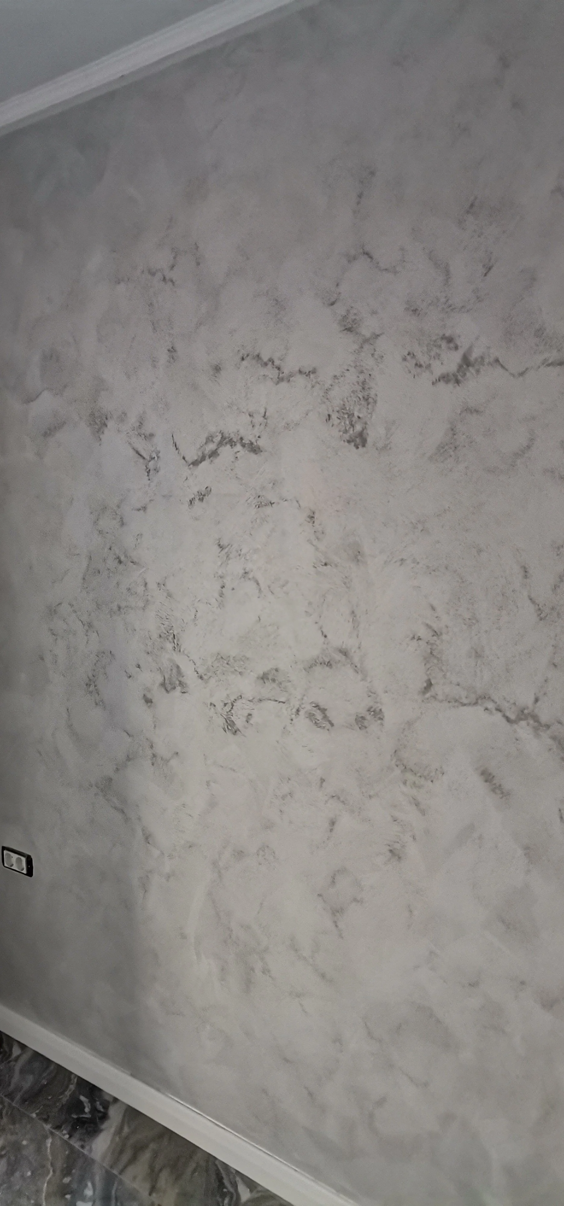 Close-up of a textured grey wall with white accents and a white baseboard at the bottom.