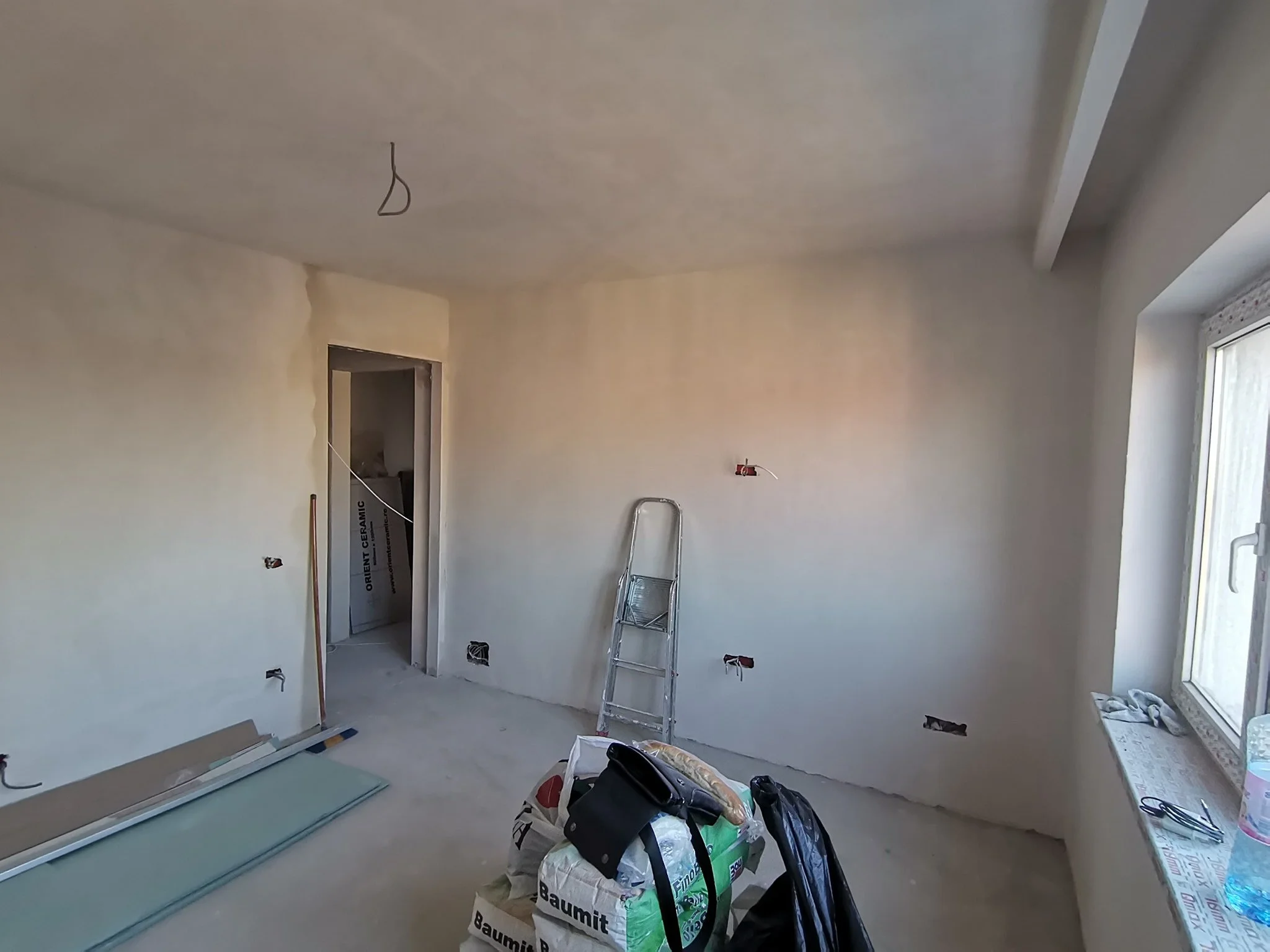 Room under construction with unfinished walls, a step ladder, construction tools and materials, and a window.