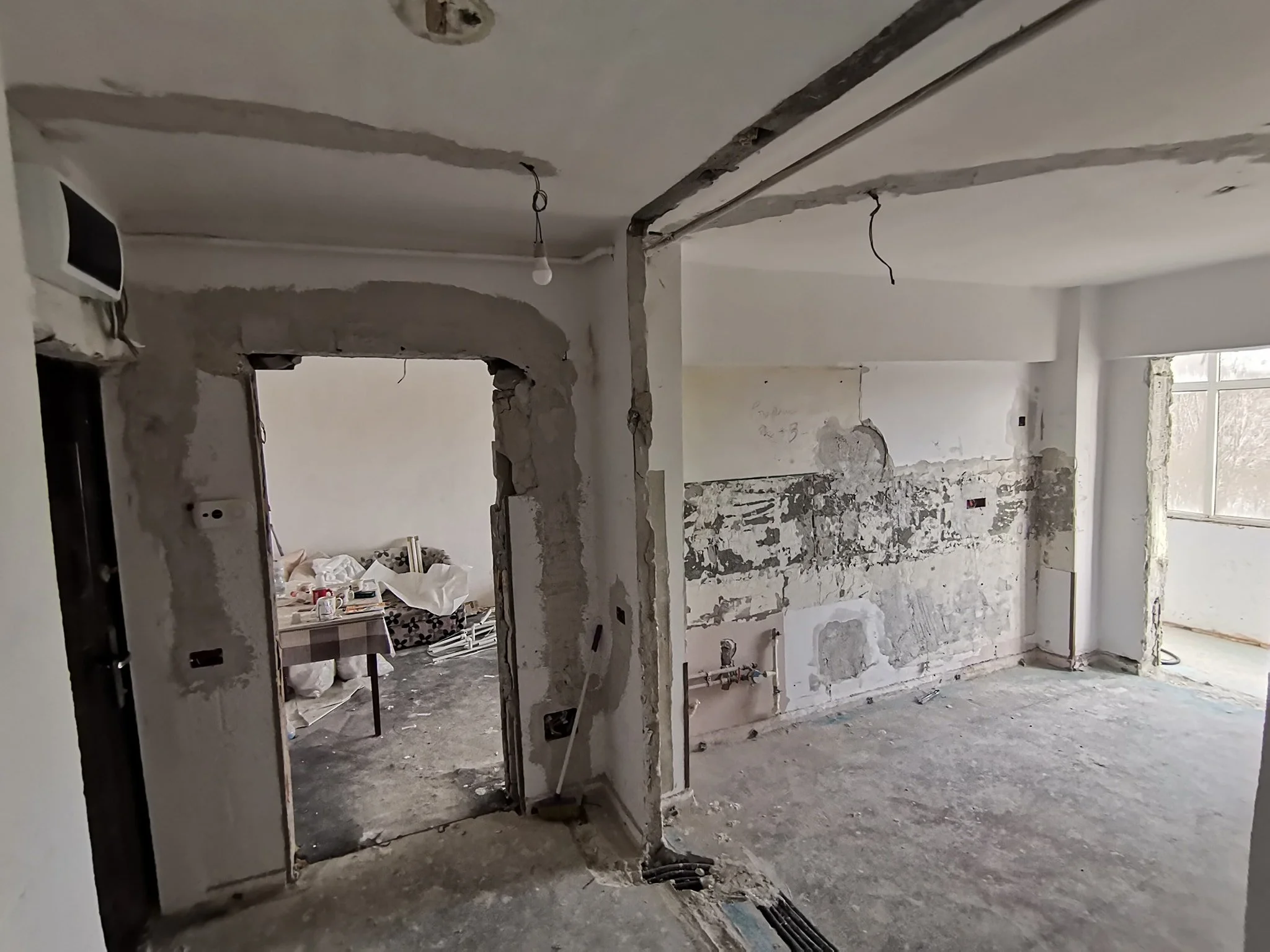 Interior of a room under renovation with exposed walls and ceiling, construction debris on the floor, and unfinished electrical wiring hanging from the ceiling.