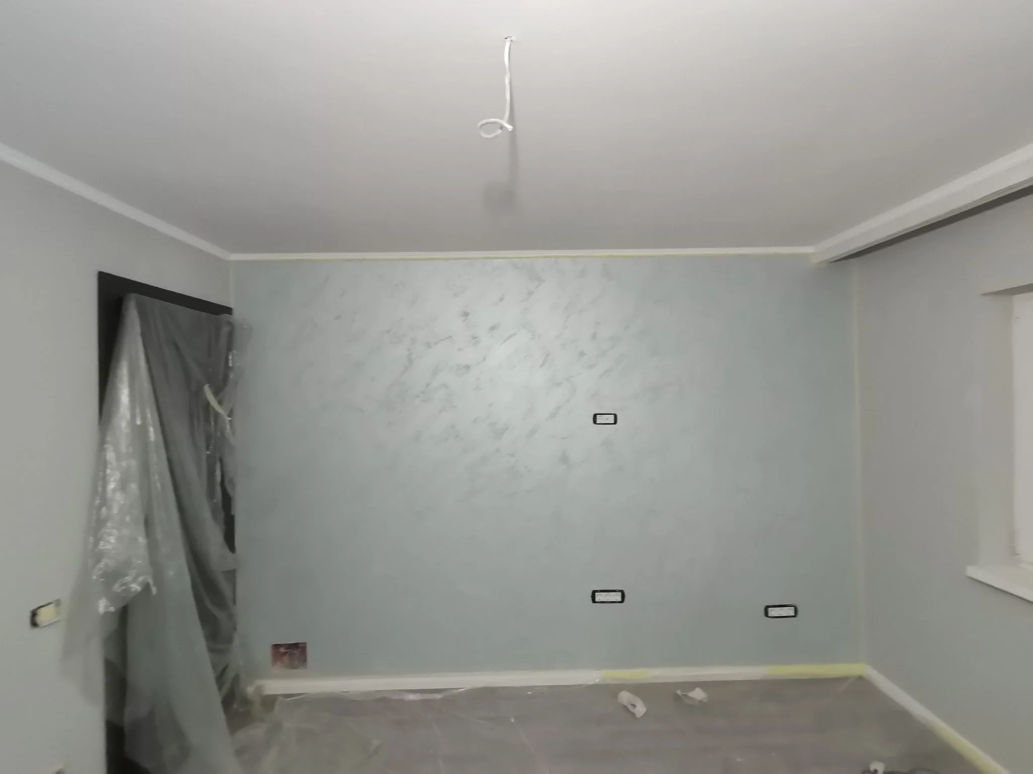 Room under renovation with plastic-covered furniture, construction tools, and electrical outlets on the wall.