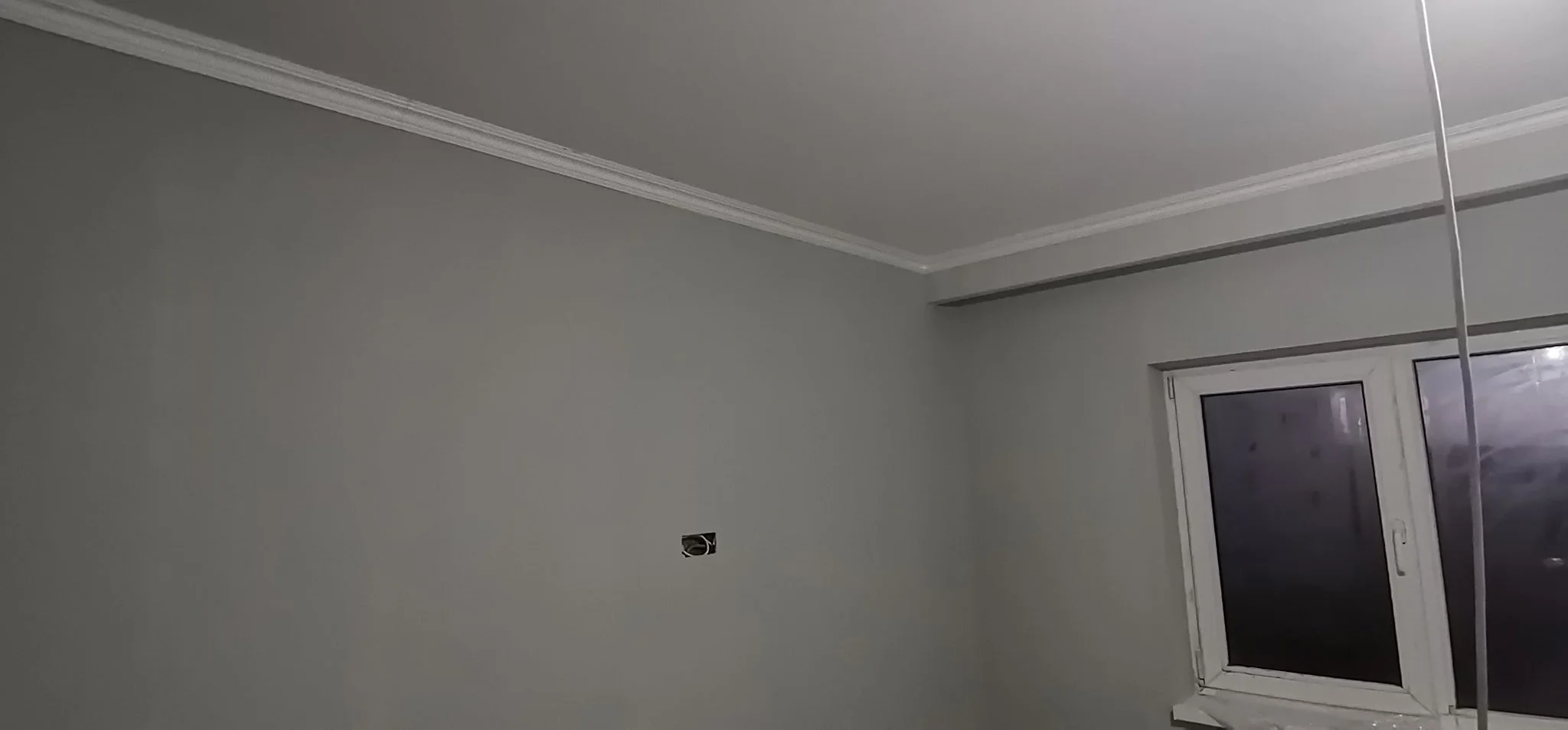 Empty room with gray walls, a window, and an electrical outlet, possibly under construction or renovation.