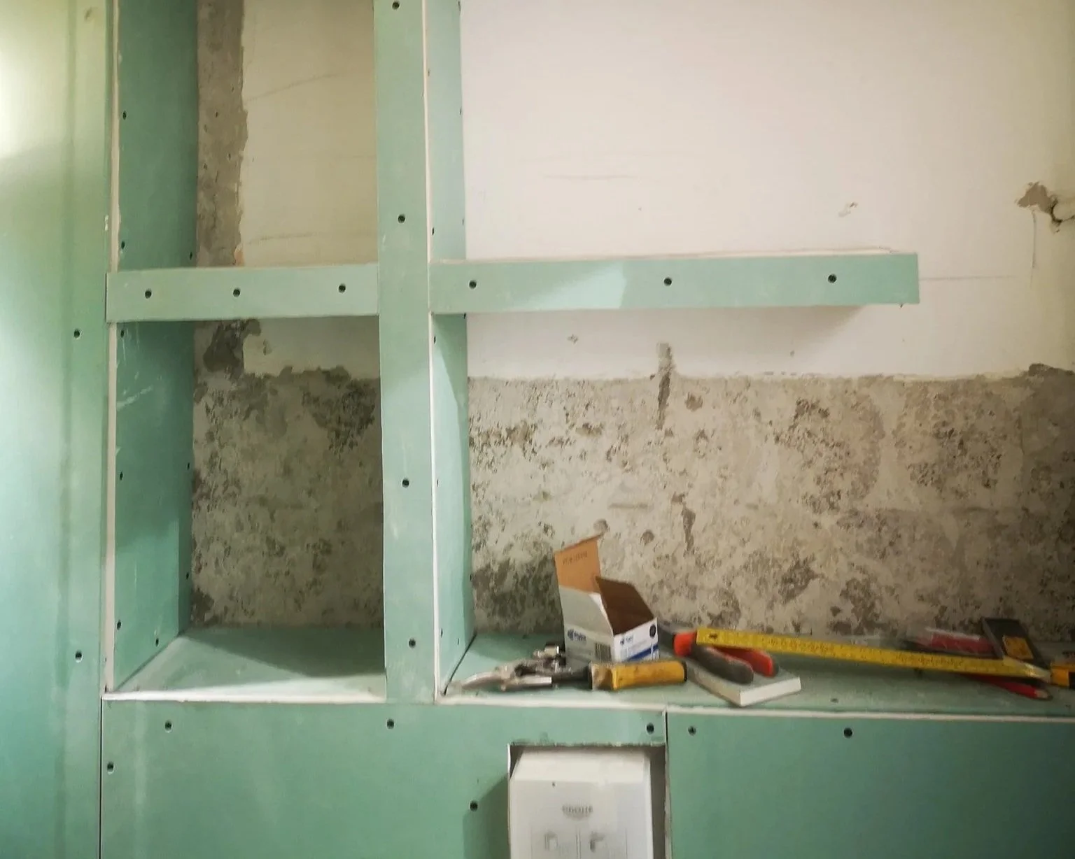 Construction site with green drywall framing, tools, and a partially finished wall.
