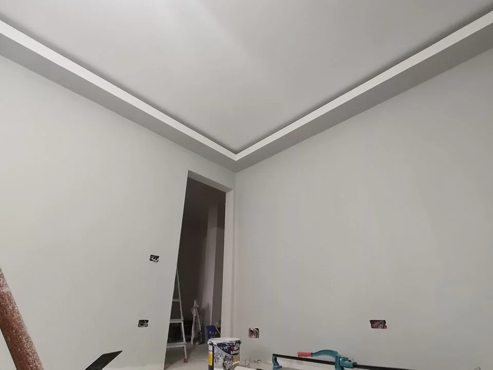 Interior room with recently painted white walls and ceiling, drywall holes for outlets, construction tools, and a ladder in the doorway.
