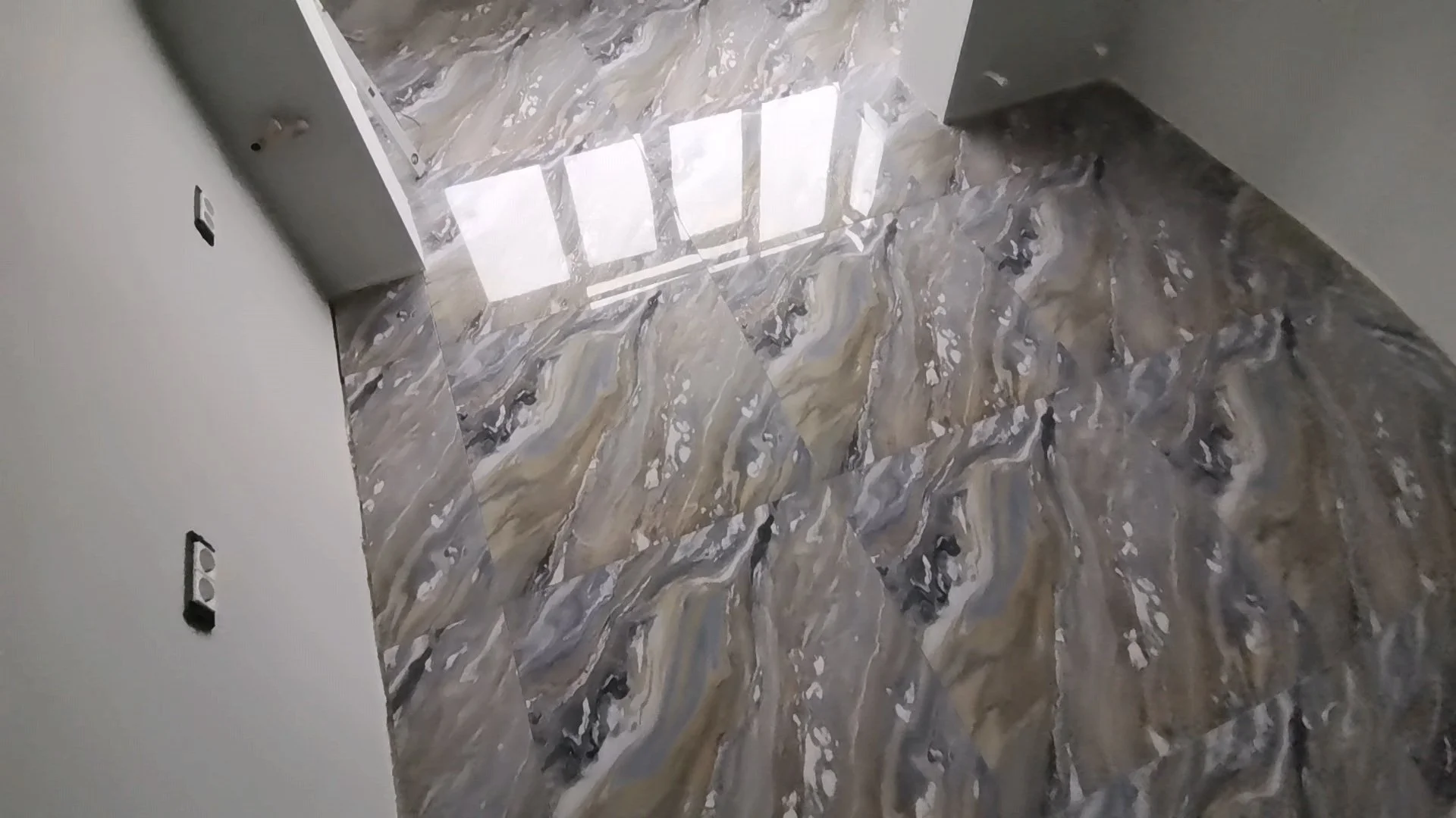 Empty room with marble flooring and a window reflecting sunlight