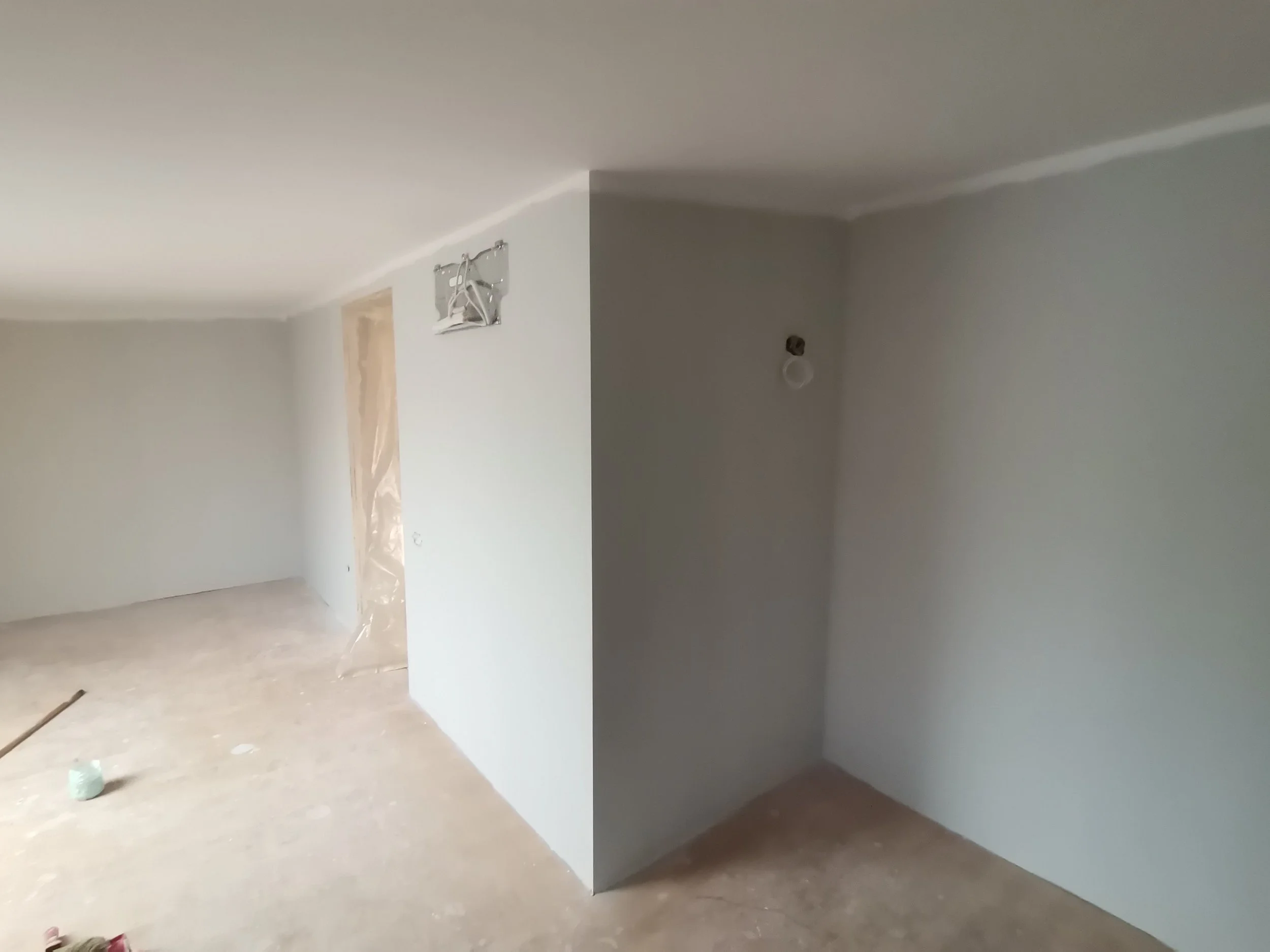Interior of a room under construction with walls painted light gray, doorway covered with plastic sheeting, and drywall installation in progress.