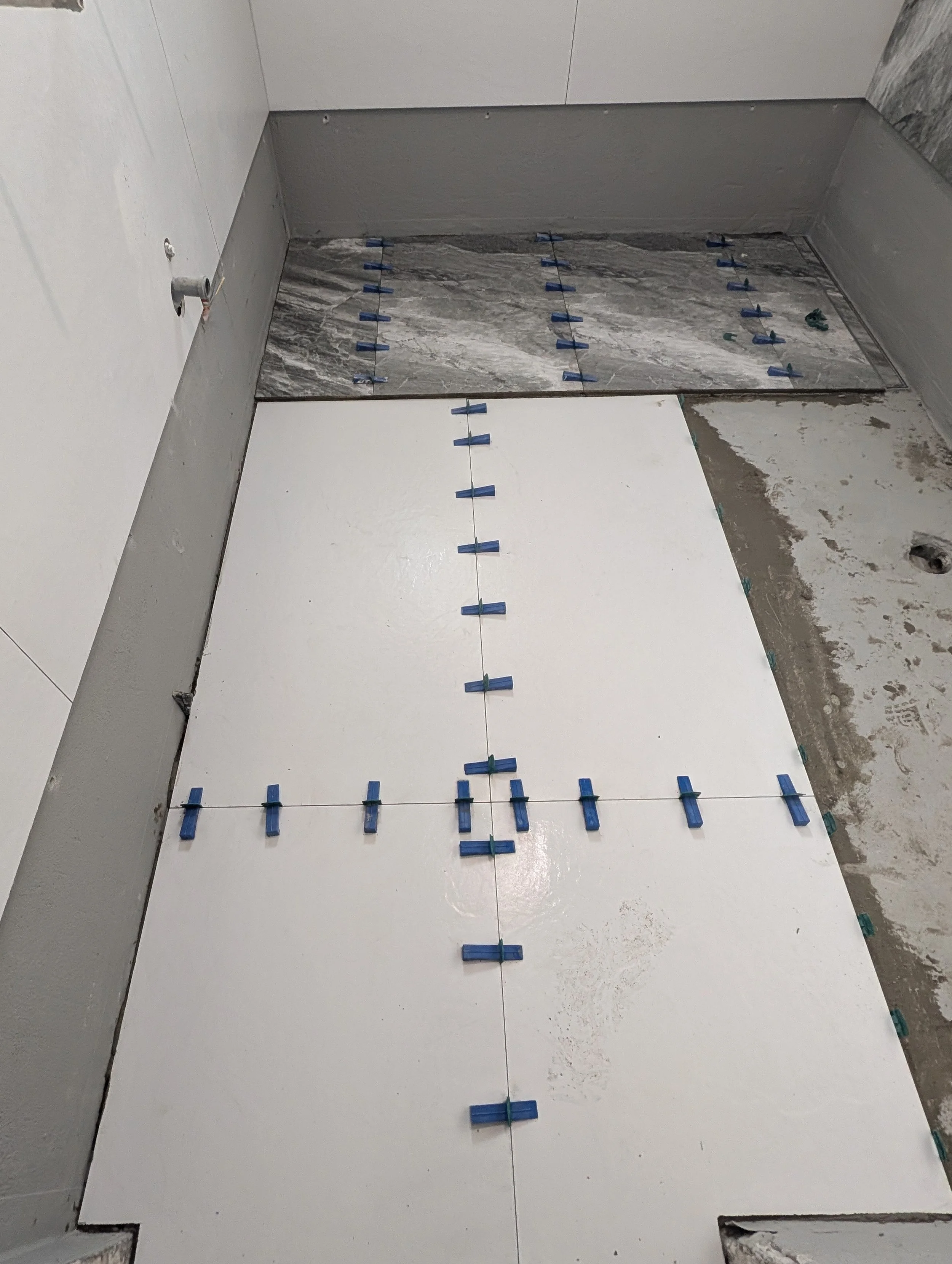 Construction site of a bathroom showing tiled floor, partially installed wall tiles, and renovation materials.