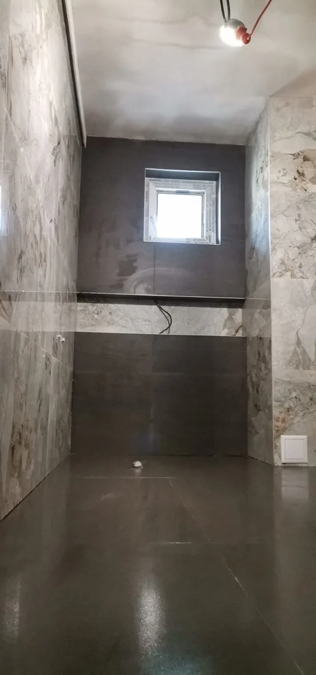 Interior of an unfinished room with concrete walls, a small window, and a polished floor, with electrical wiring and a light fixture hanging from the ceiling.