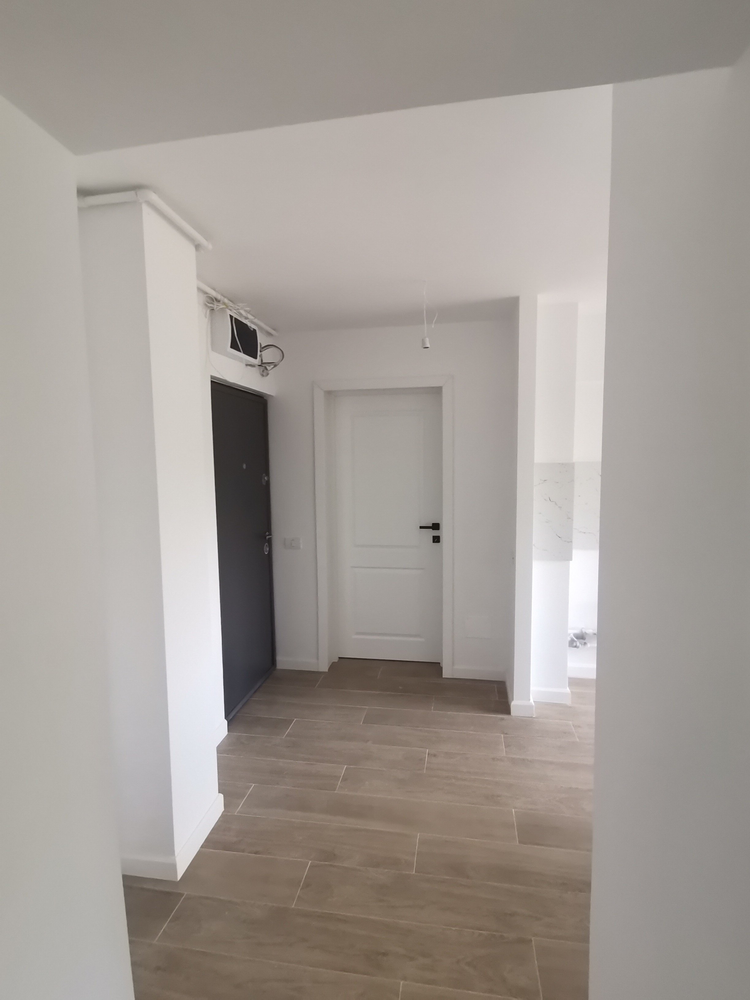 Empty hallway with white doors, tiled wooden flooring, and an air conditioning unit on the wall.