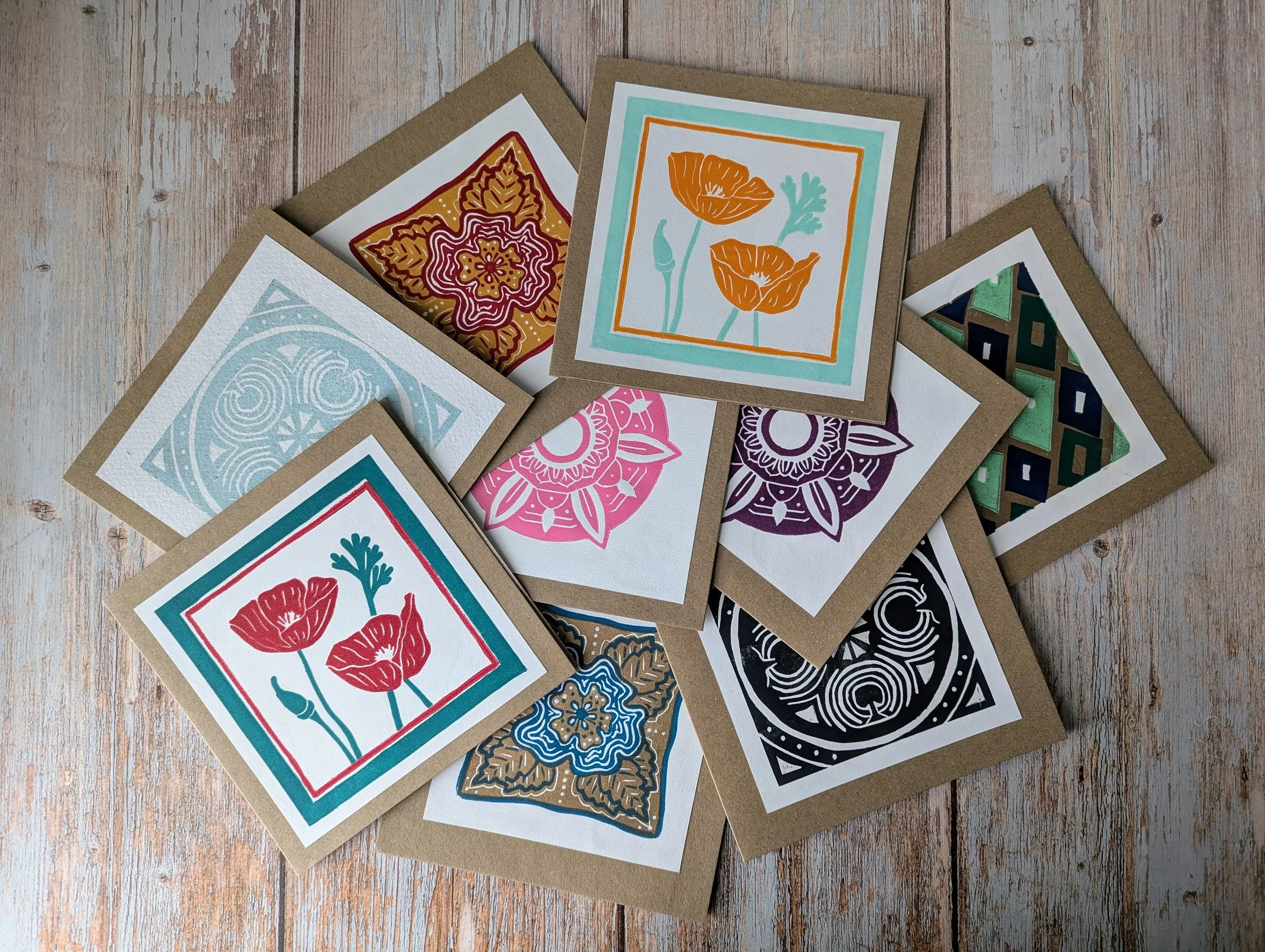 A collection of colorful hand printed greeting cards with floral and geometric designs spread out on a wooden surface.