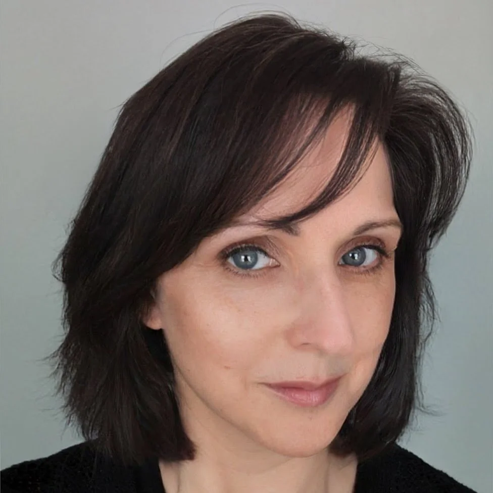 A woman with shoulder-length dark brown hair and blue eyes looking at the camera with a neutral expression.