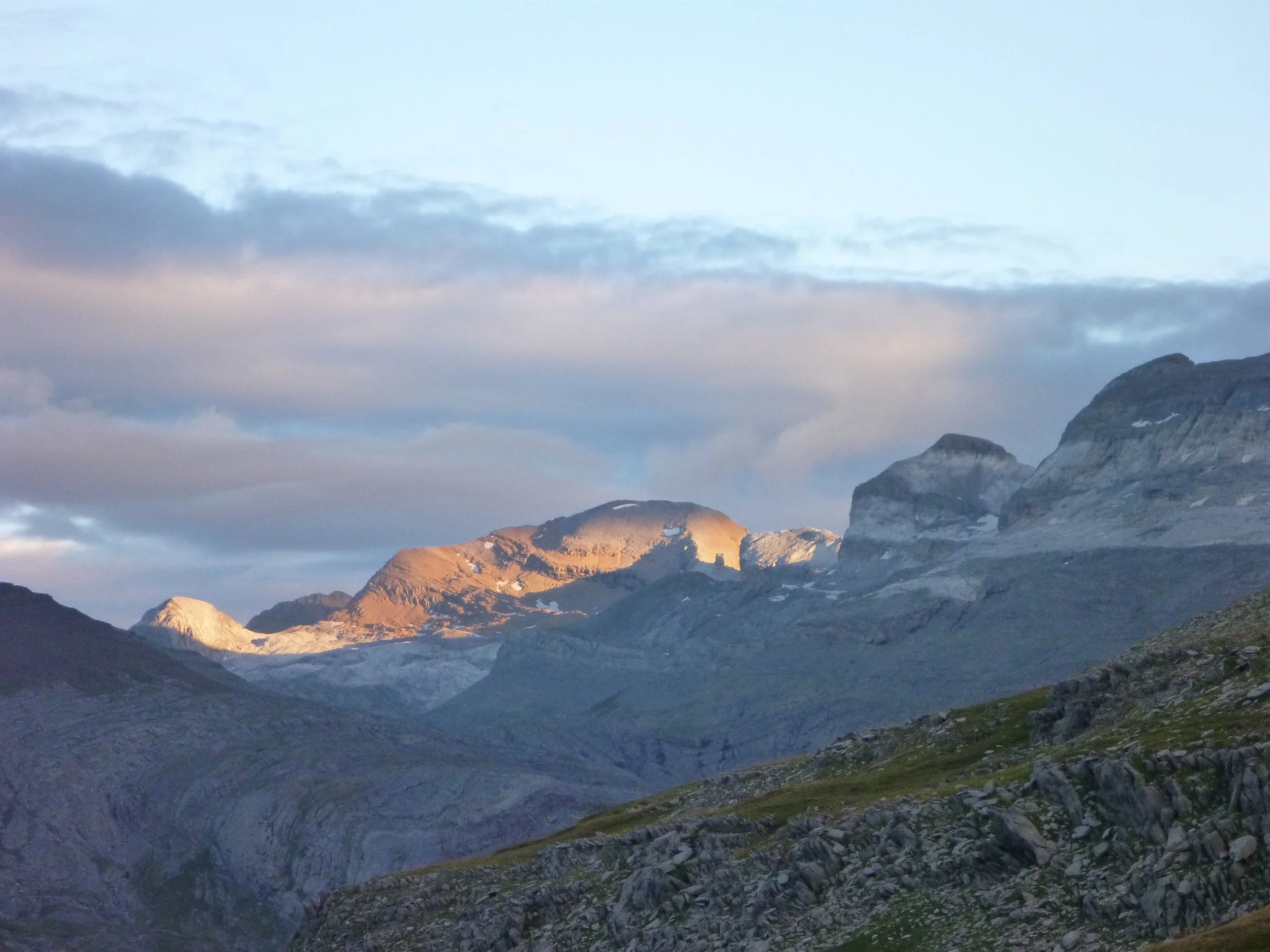 Montañas y valle cubierto de roca y vegetación con nubes en el cielo y una luz del atardecer