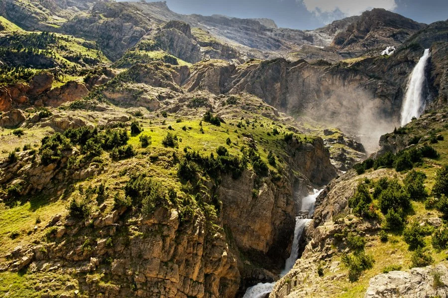 Paisaje de montañas con cascadas y vegetación verde.