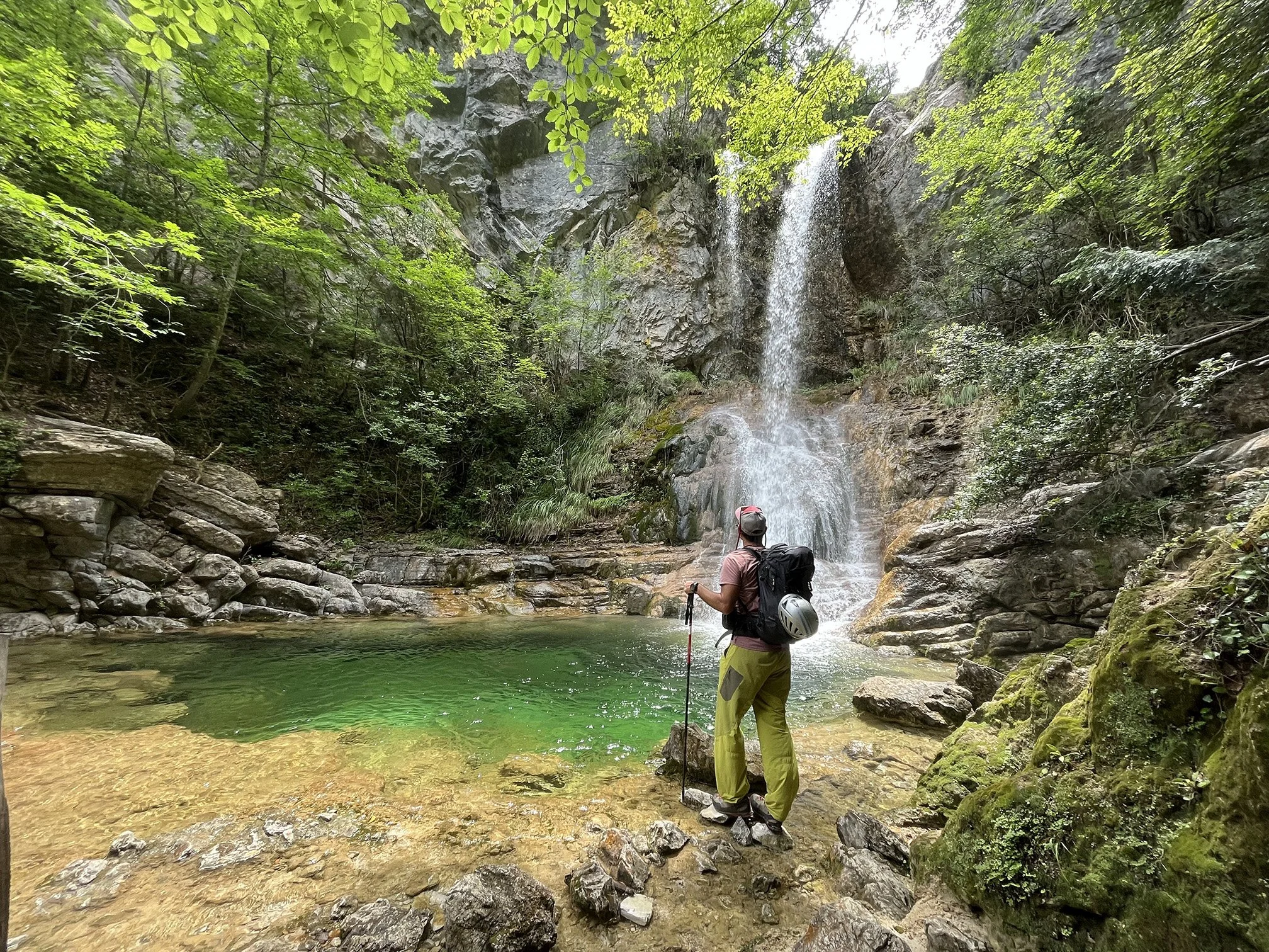 Persona con mochila y casco observando una cascada en un entorno forestal