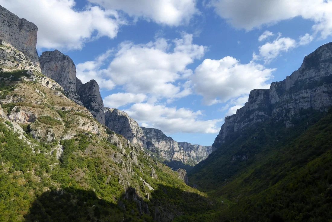 Vista de un cañón con paredes rocosas y vegetación, cielo con nubes.