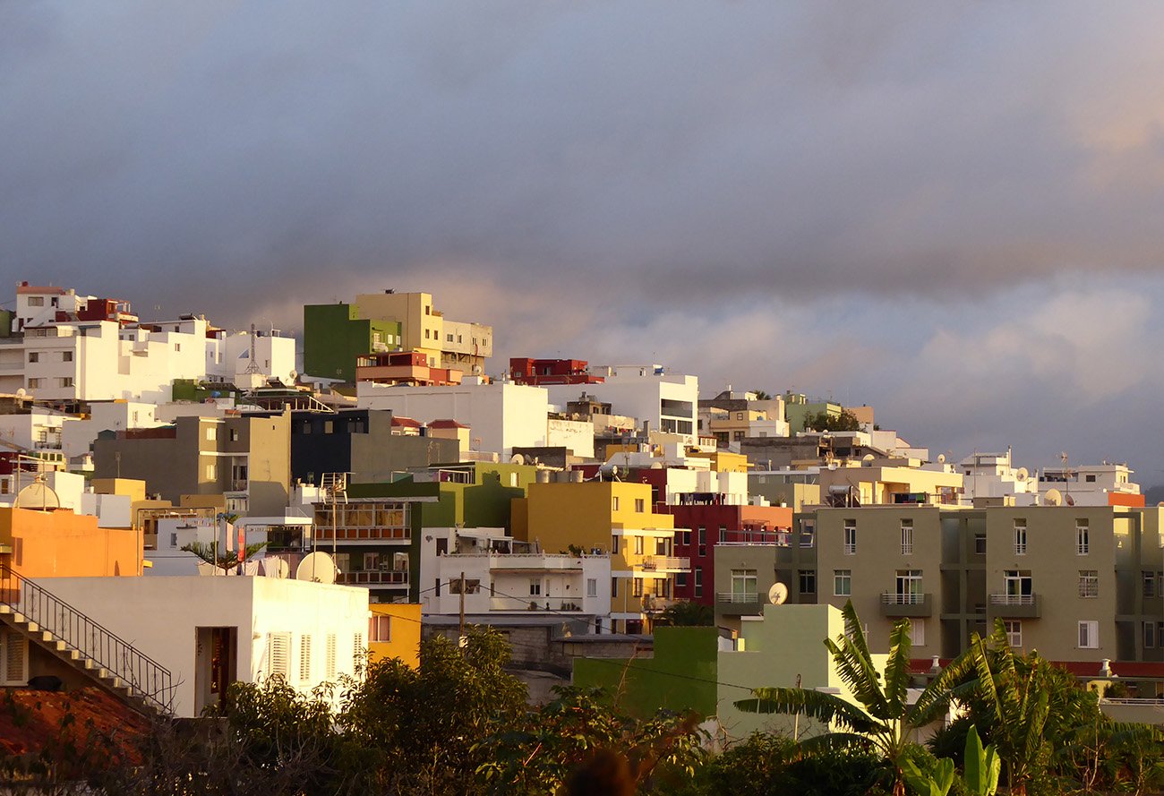 Vista de una ciudad con casas de colores en una colina frente a un cielo nublado al atardecer.