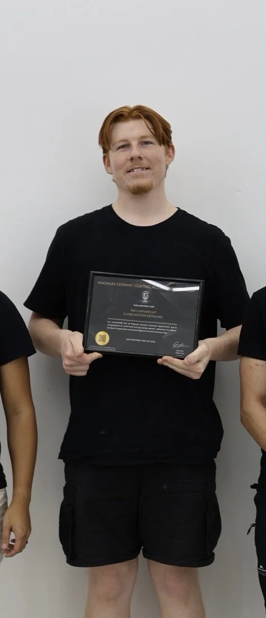 A young man with red hair and a beard holding a certificate, standing against a white wall.