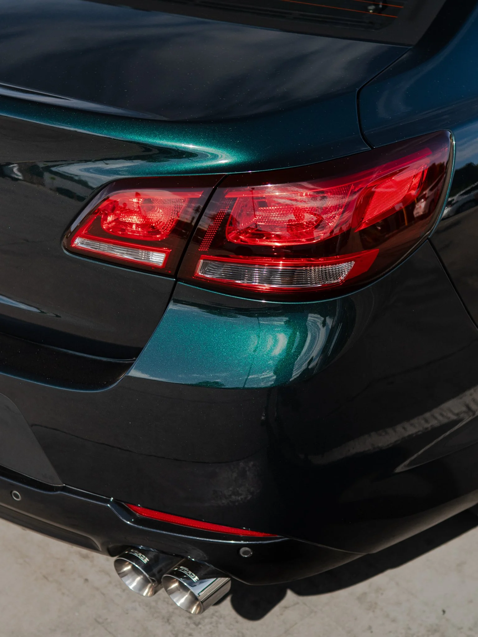 Close-up of the rear end of a black sports car showing taillights and dual exhaust pipes.