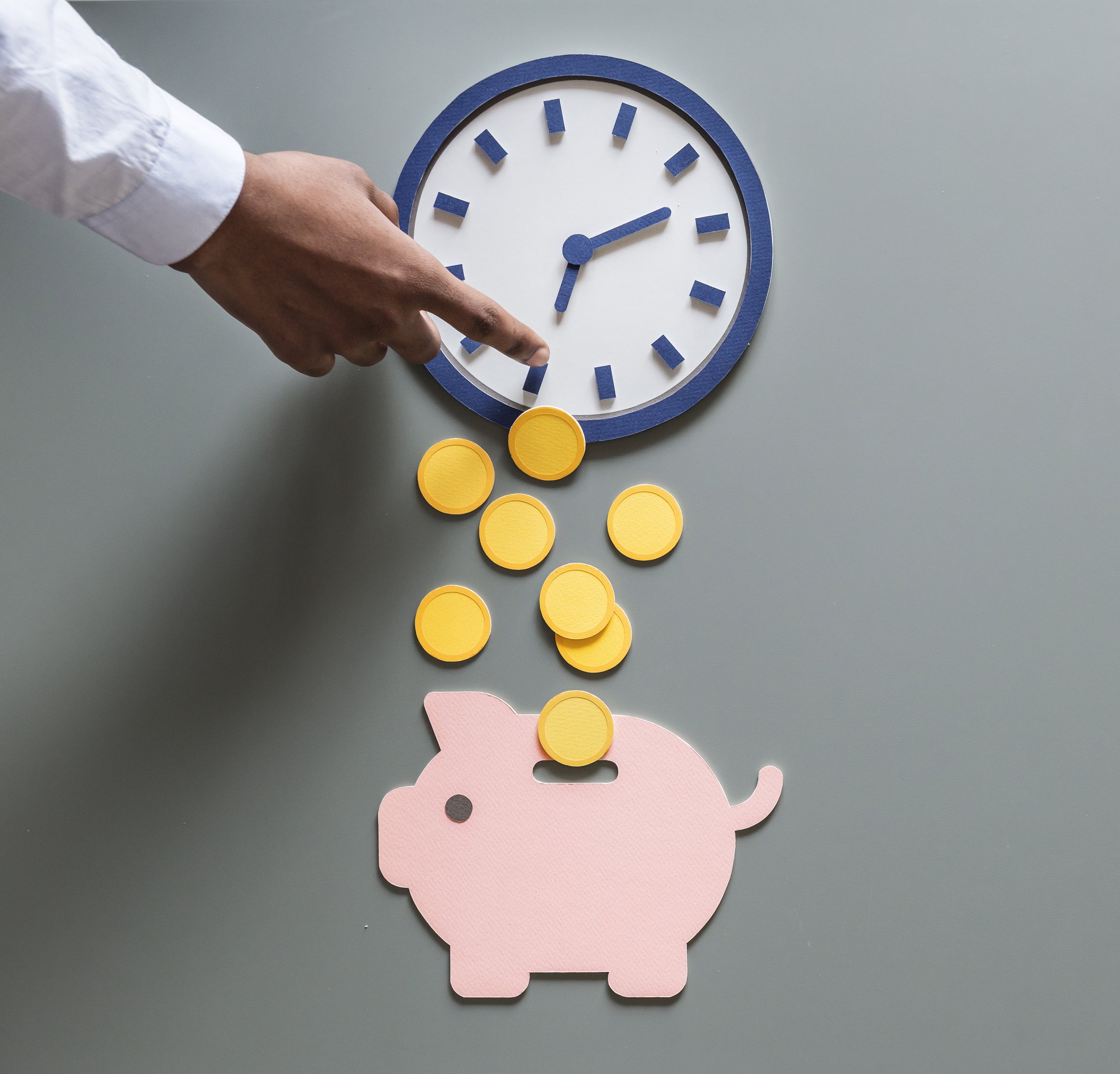 A pink paper pig with a coin on top, a clock with blue hour and minute hands, and yellow coins falling from its mouth.