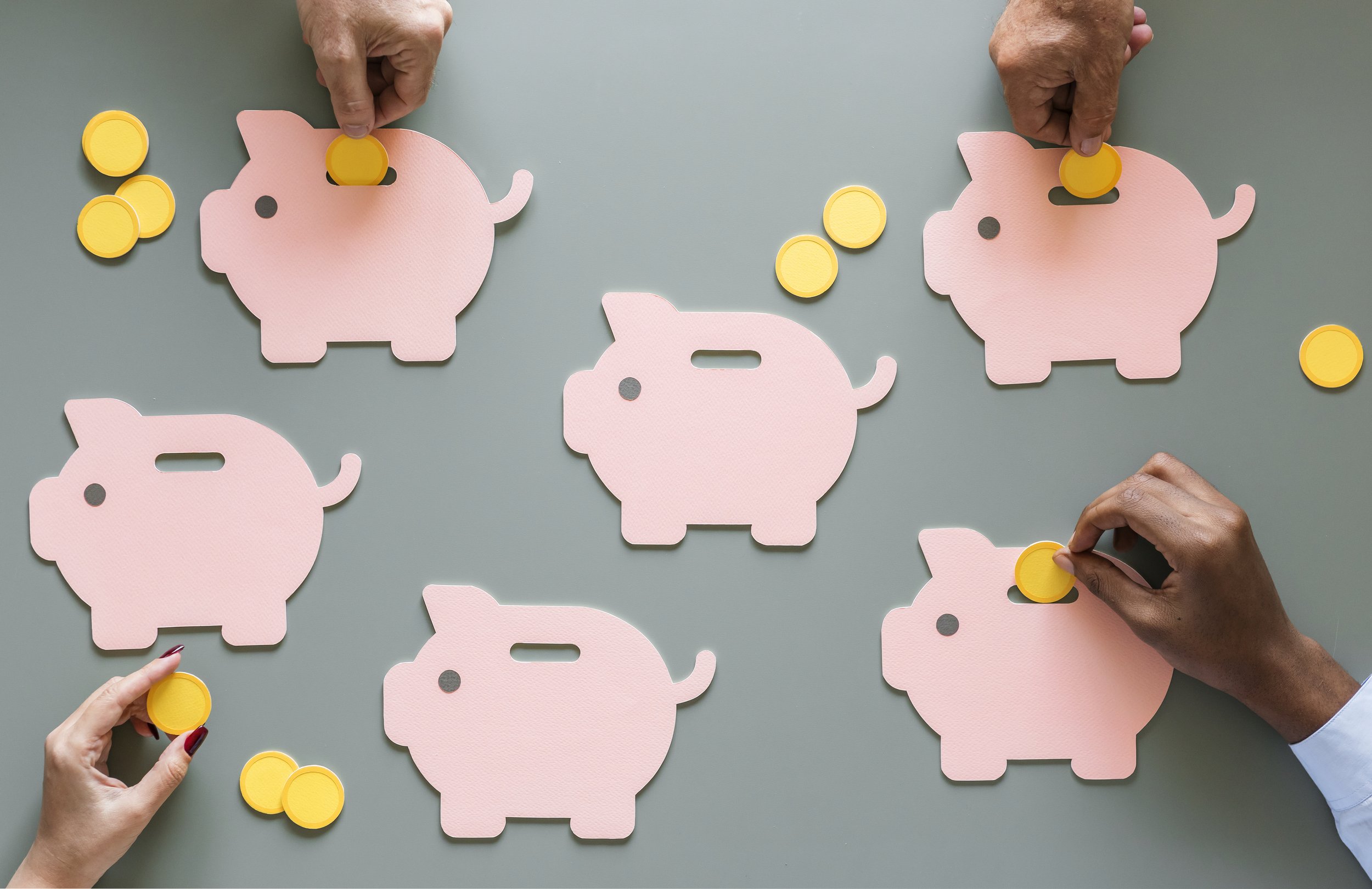 People are placing yellow coins into pink pig-shaped cutouts on a gray surface.