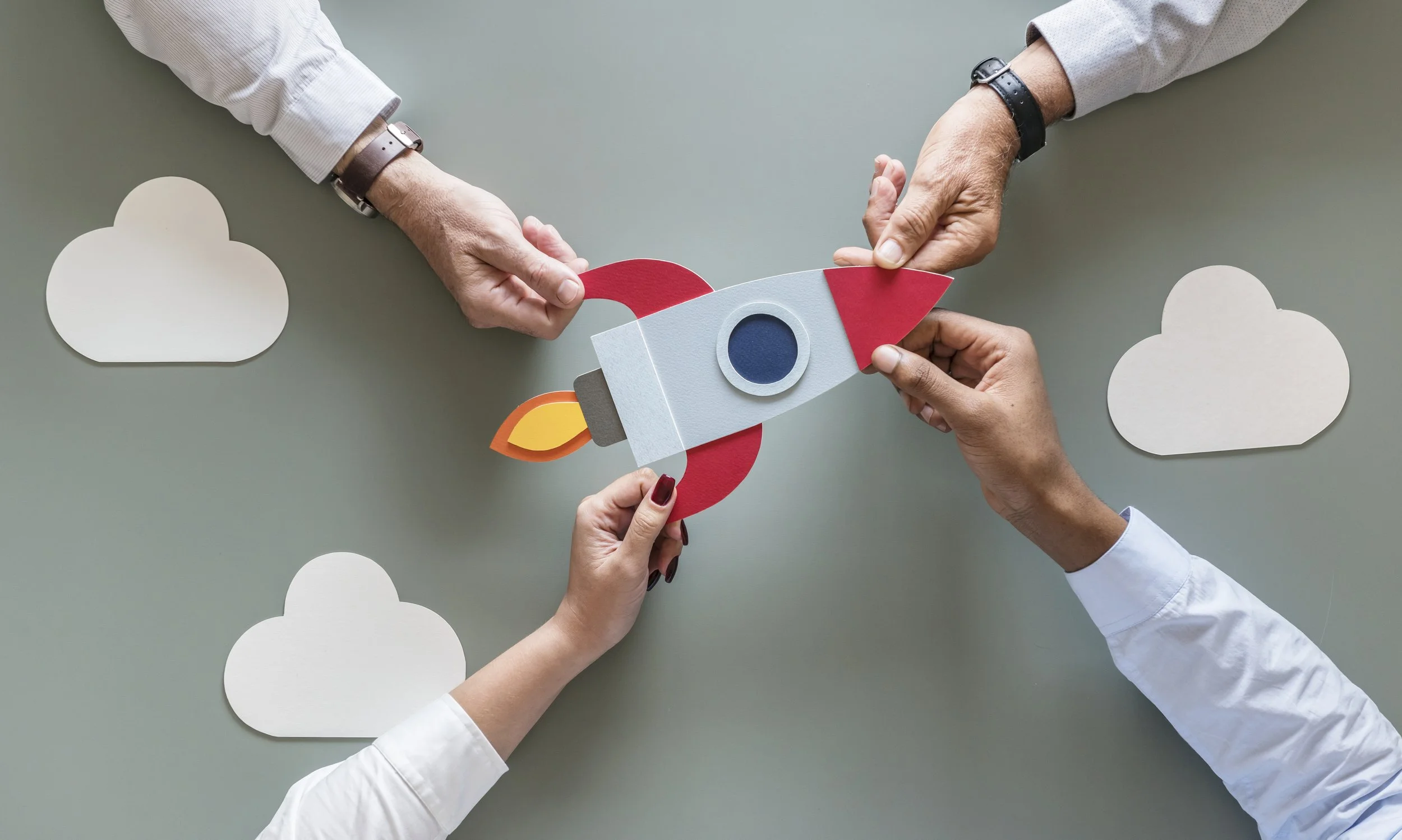 Three people hold a paper craft rocket in front of paper clouds on a green background.