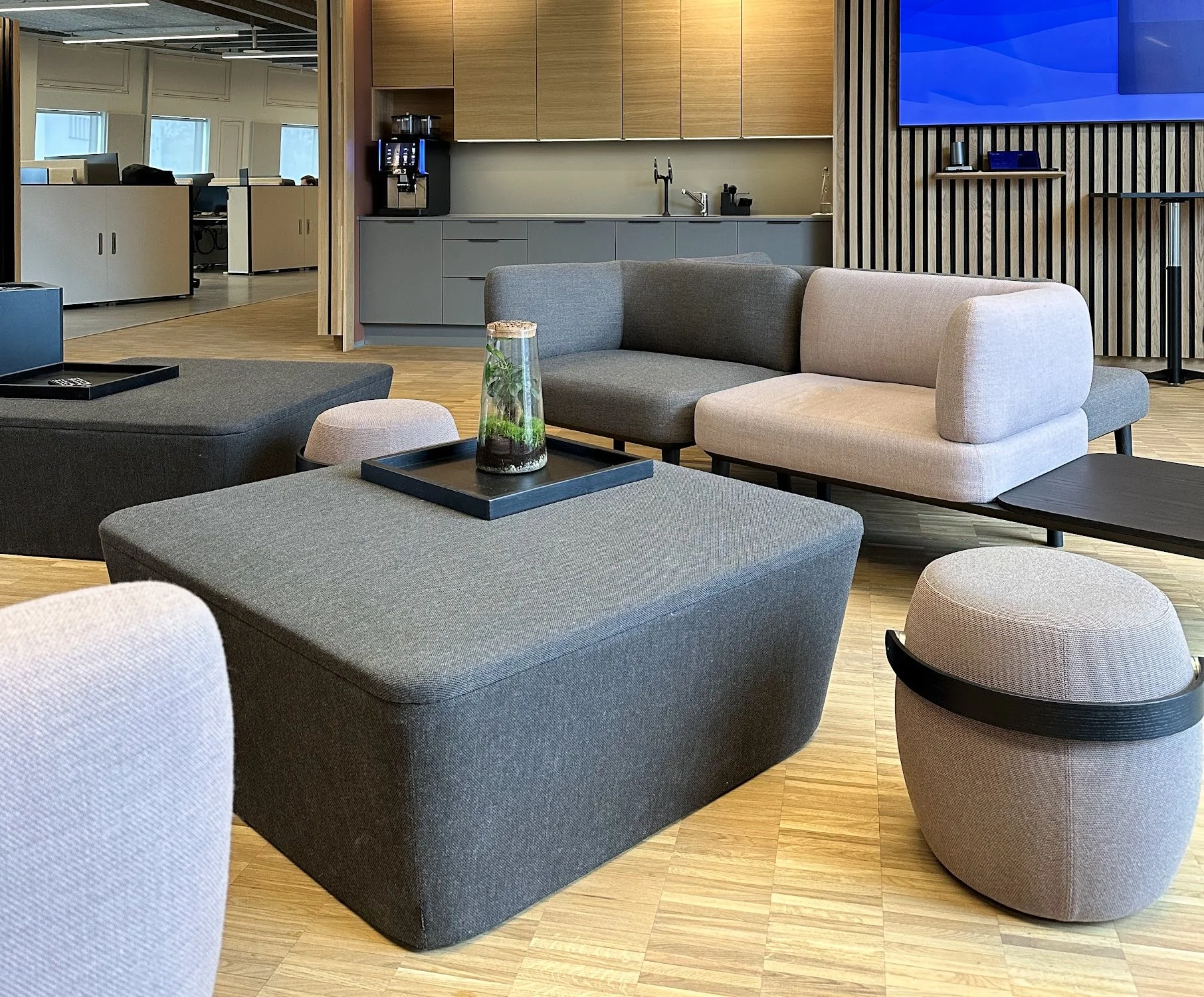 Moderne kontor- og loungeområde med sofaer, små stoler, et bord med plante, og et kjøkkenområde i bakgrunnen.