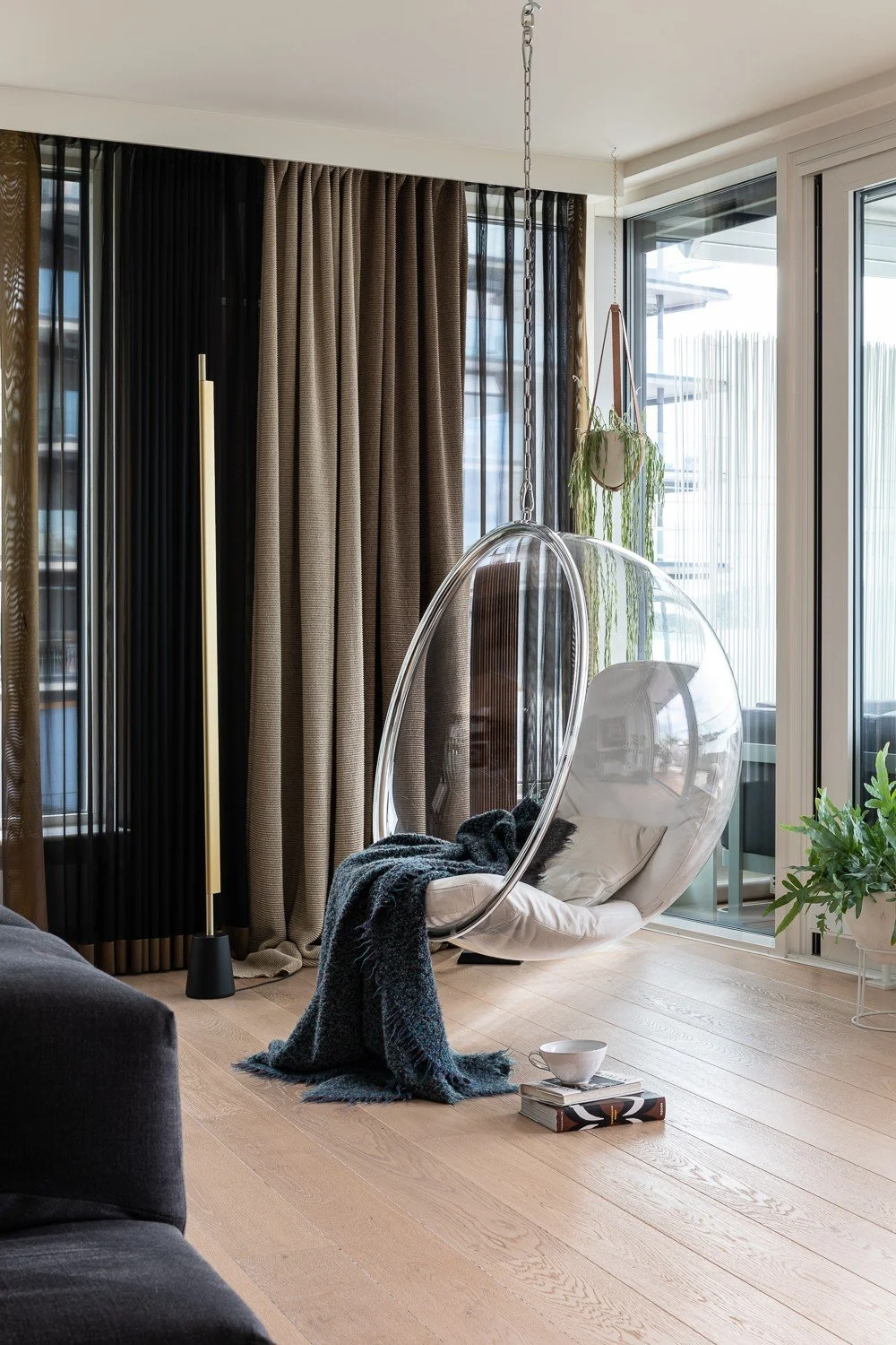 Hengende stol ved vinduet, gardiner i flere lag og gulvlampe i messing, leilighet på Tjuvholmen