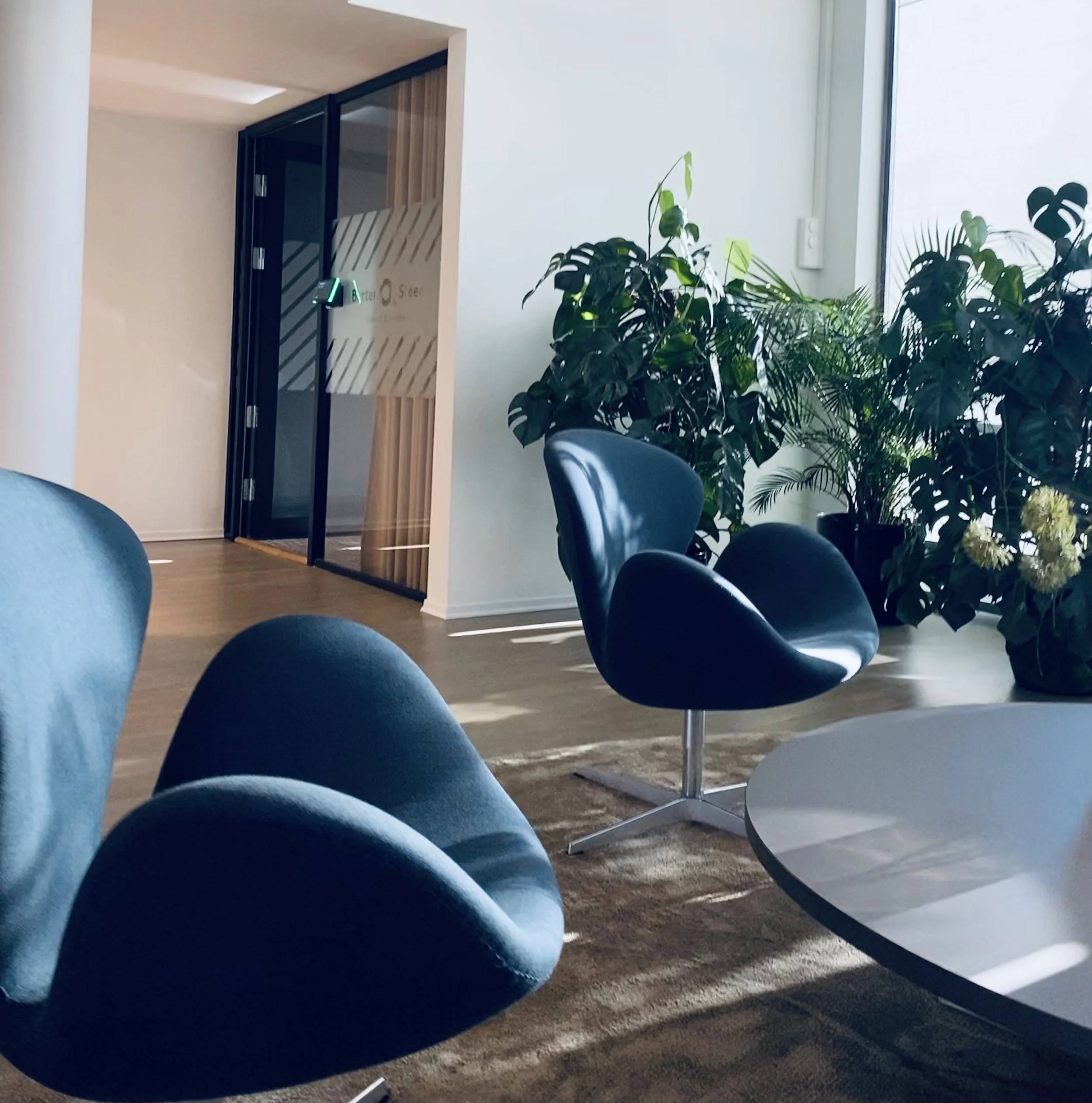 Innendørs møteområde med flere blå stoler og grønne planter nær store vinduer.