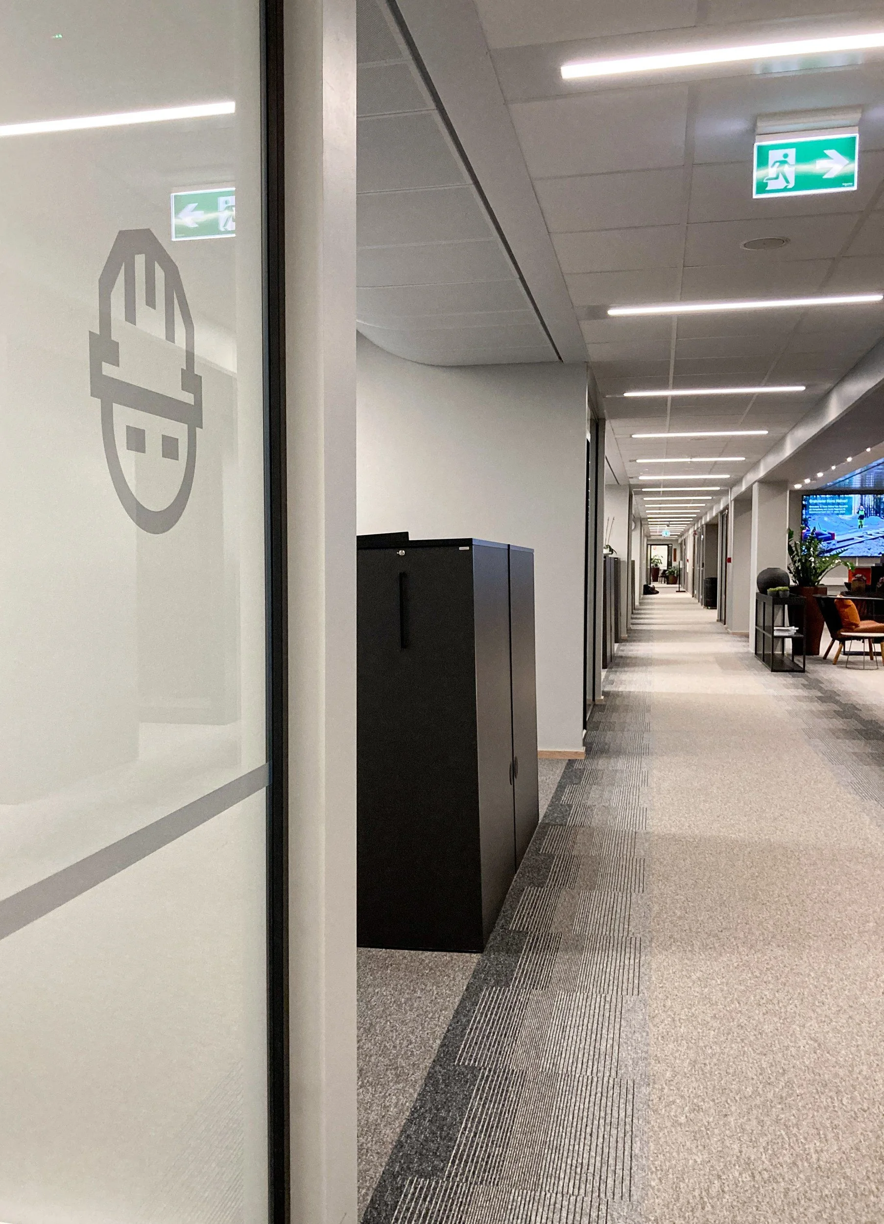 Korridor med foliedekor av hjelmsymbol på glass og teppefliser som går fra lyst til mørkt, Spordrift