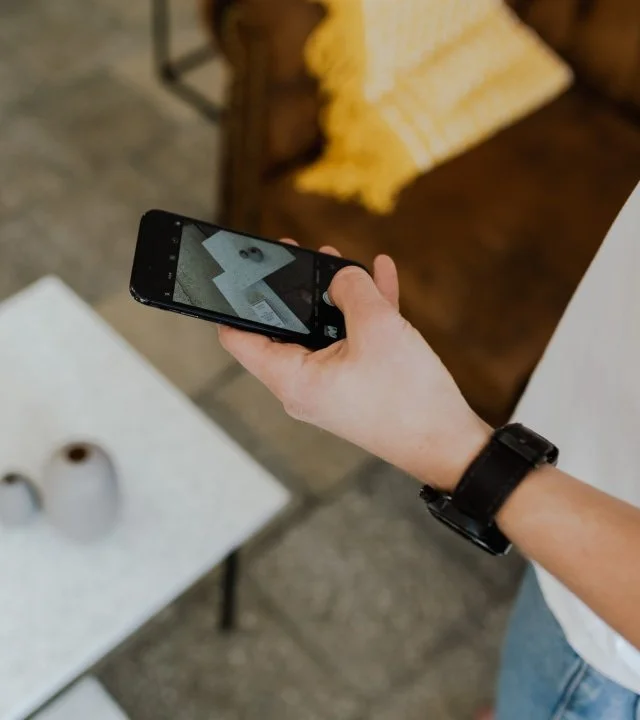 Person taking a photo of a paper with a face on it using a smartphone in a cozy indoor setting.