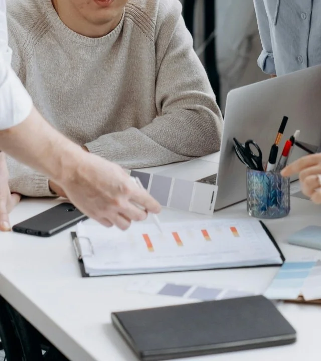 People working at a desk with documents, a laptop, and office supplies.