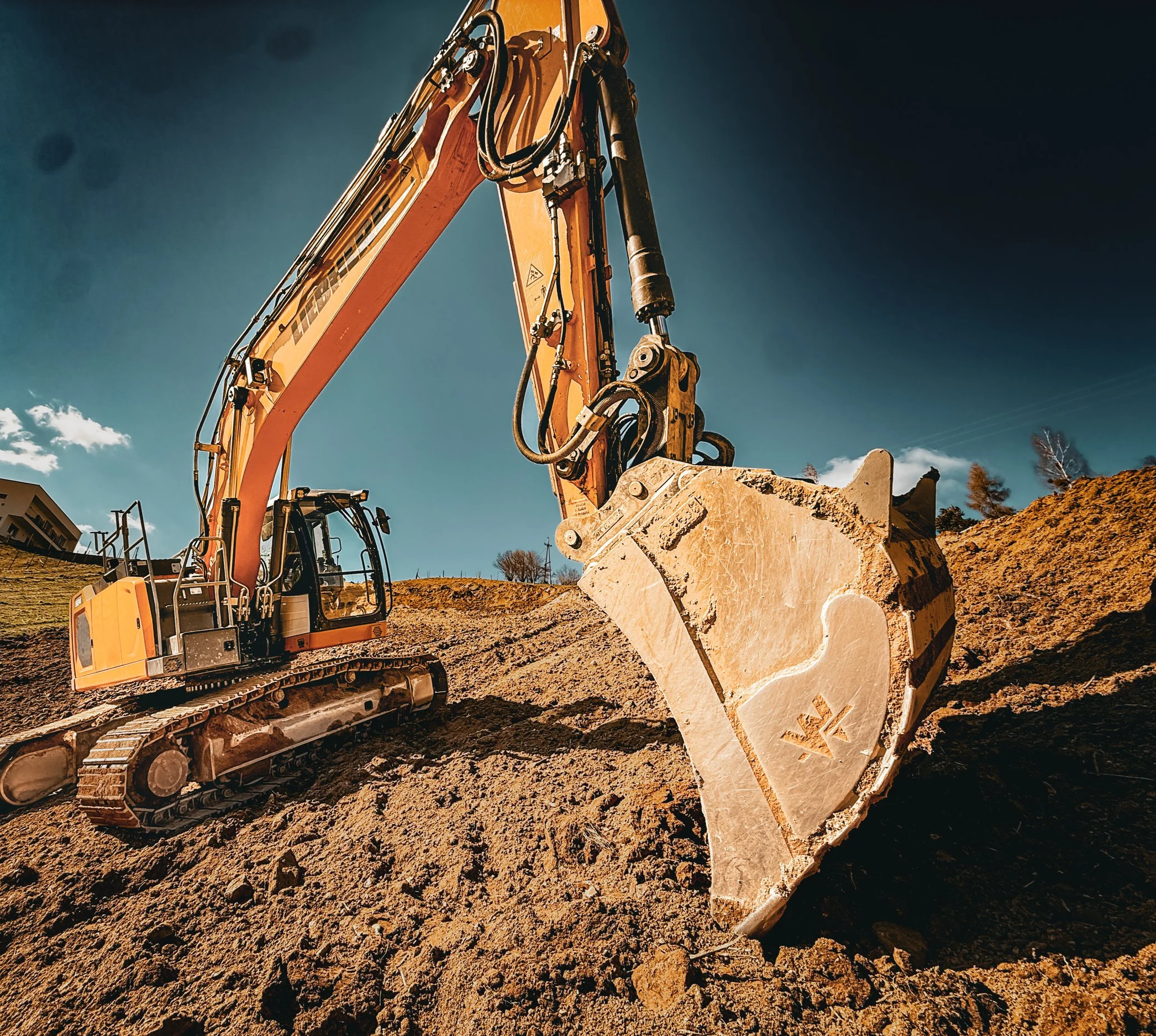 Ein gelber Bagger auf einer Baustelle, der auf unebenem Boden arbeitet, bei strahlendem Sonnenschein.