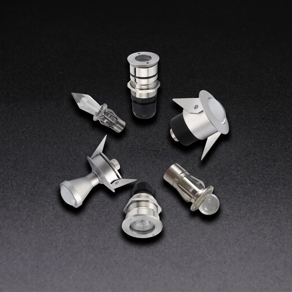 Seks små metall- og glasslupper, sannsynligvis for optikk eller lyskilder, plassert på en svart bakgrunn.