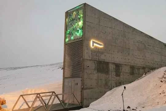 Modern betongbygning med lysende kutt i veggen, omgitt av snø, med utømmelig lys i en grønn nyanse, i kaldt vær.