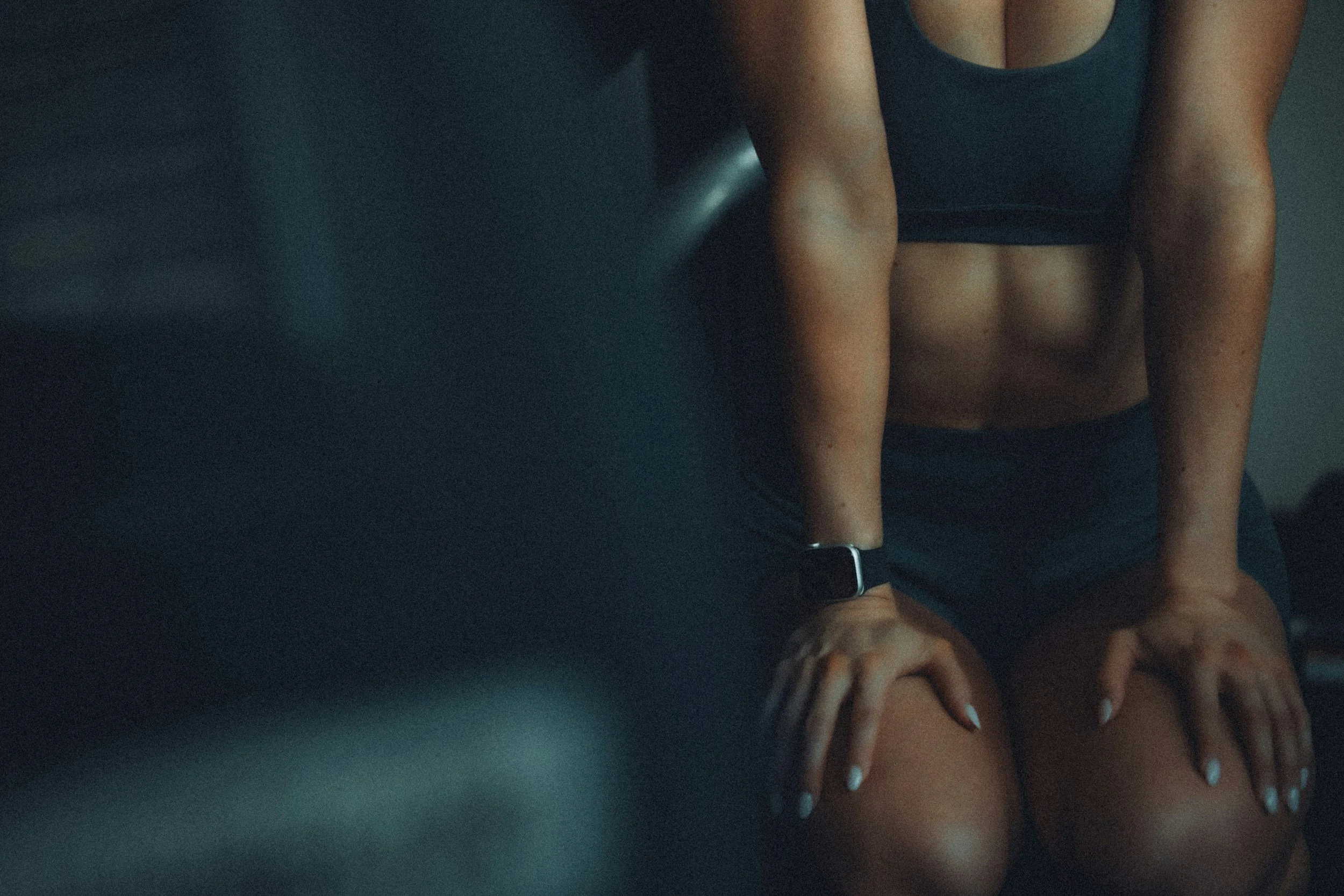 Woman in sportswear with smartwatch, in a dark setting, focusing on her toned arm and upper body.