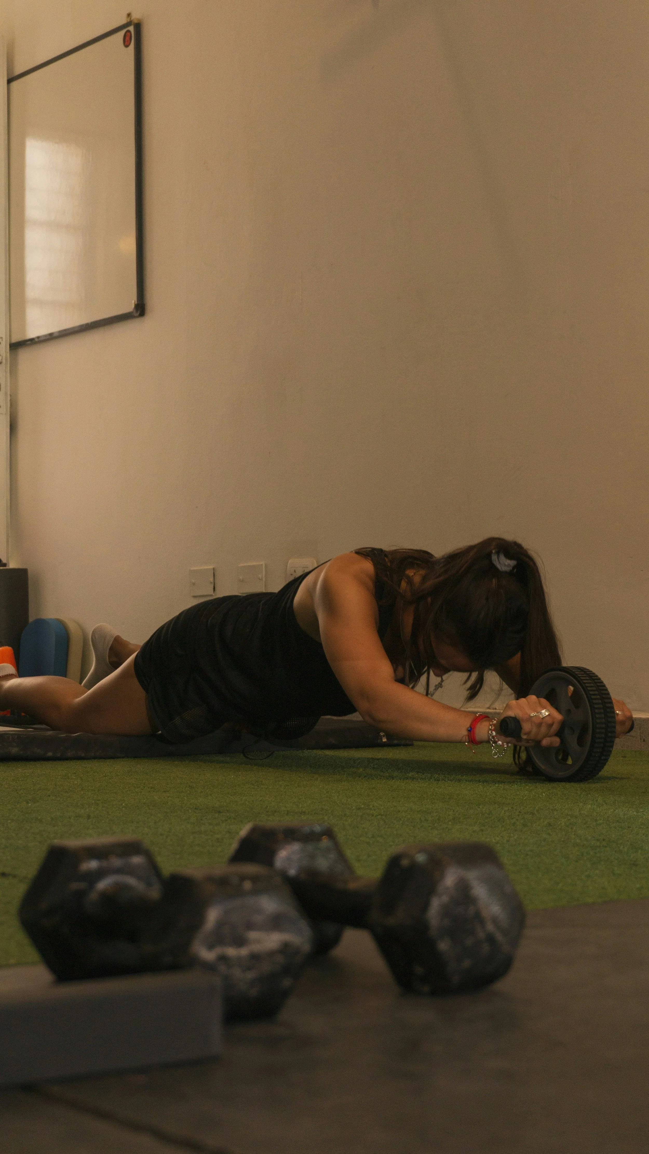 A woman performing an abdominal workout on an exercise mat using a rolling wheel in a gym.