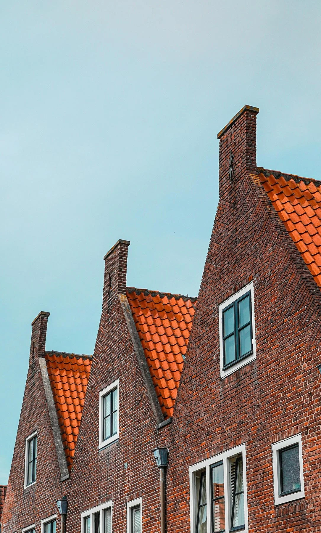 Close-up van een traditioneel rood bakstenen gebouw met een rode tegelgeschilferd dak, drie schoorstenen en witte raamkozijnen.