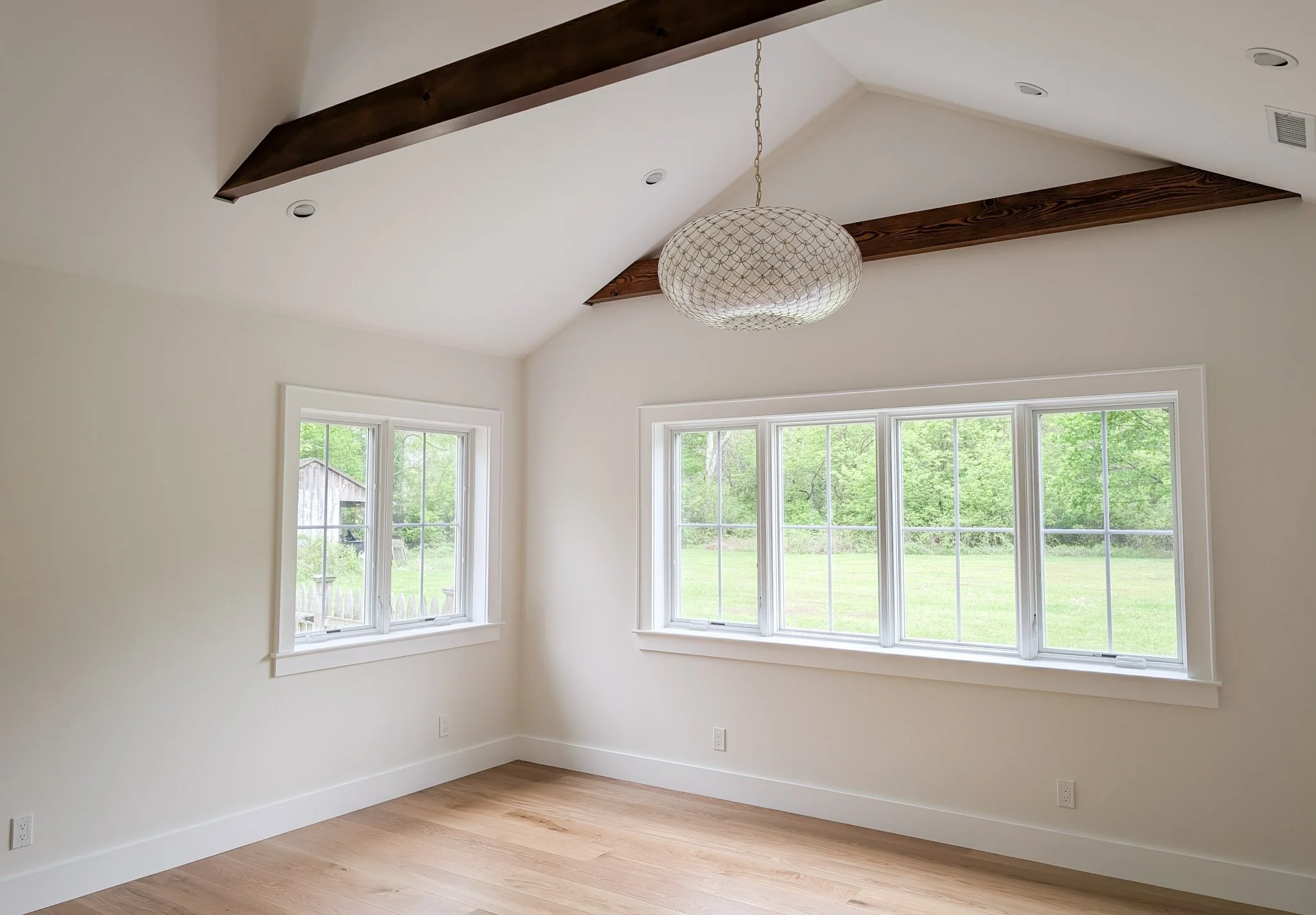 empty bedroom with large modern chandelier, wood floors, exposed beams, and white walls