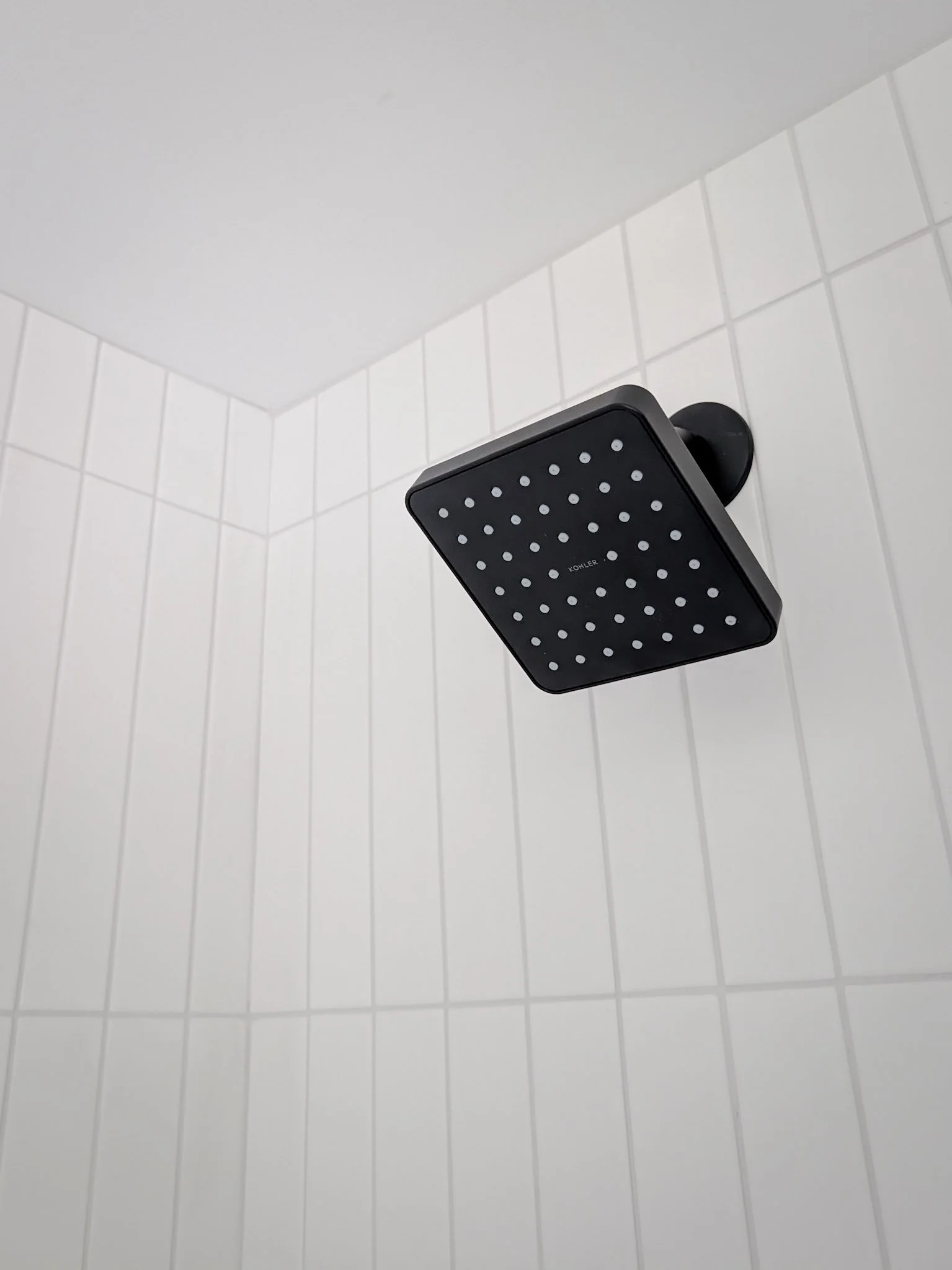 black showerhead against a white tile shower wall