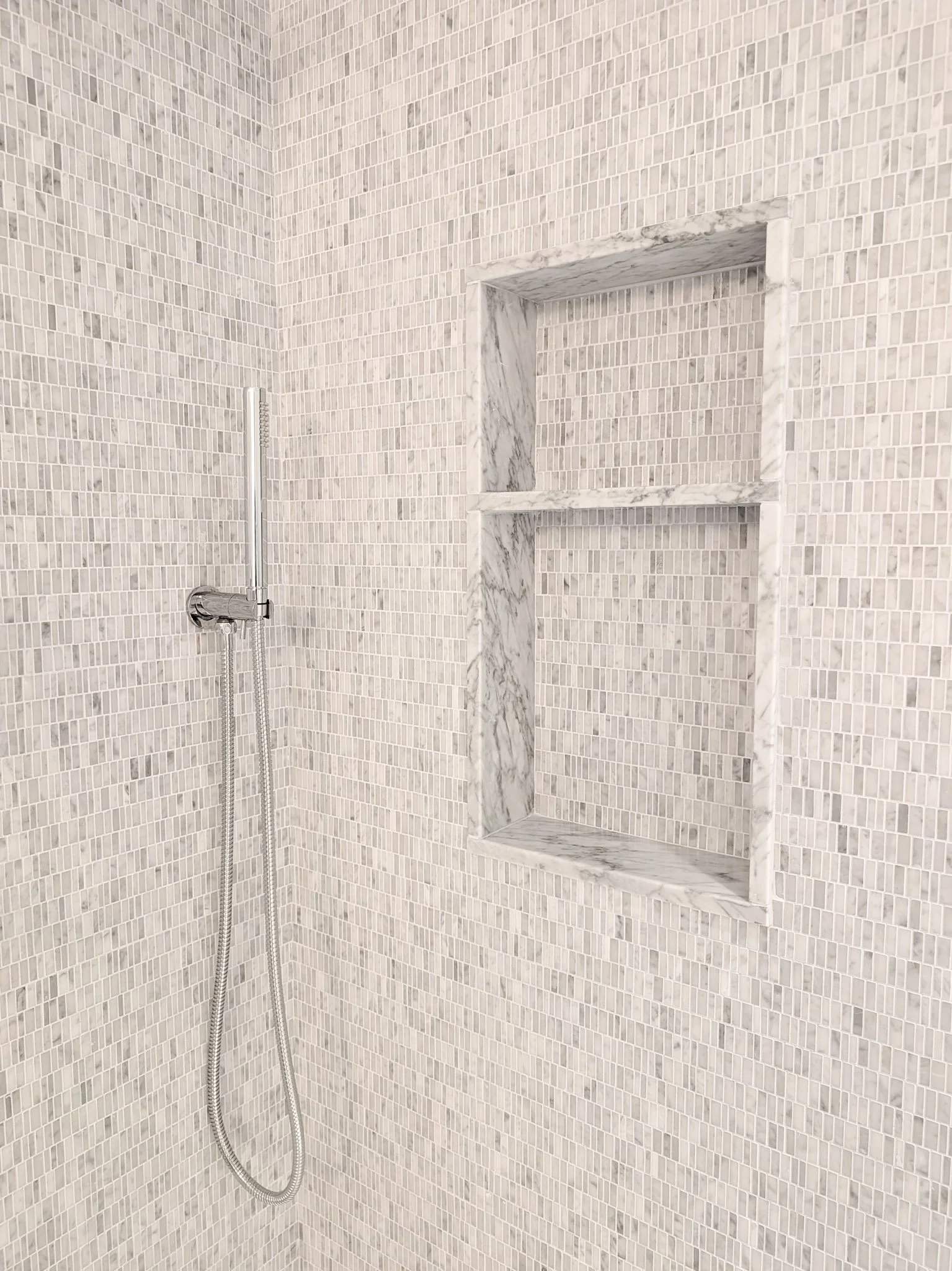 Inset marble-tiled shower shelving detail in custom bathroom