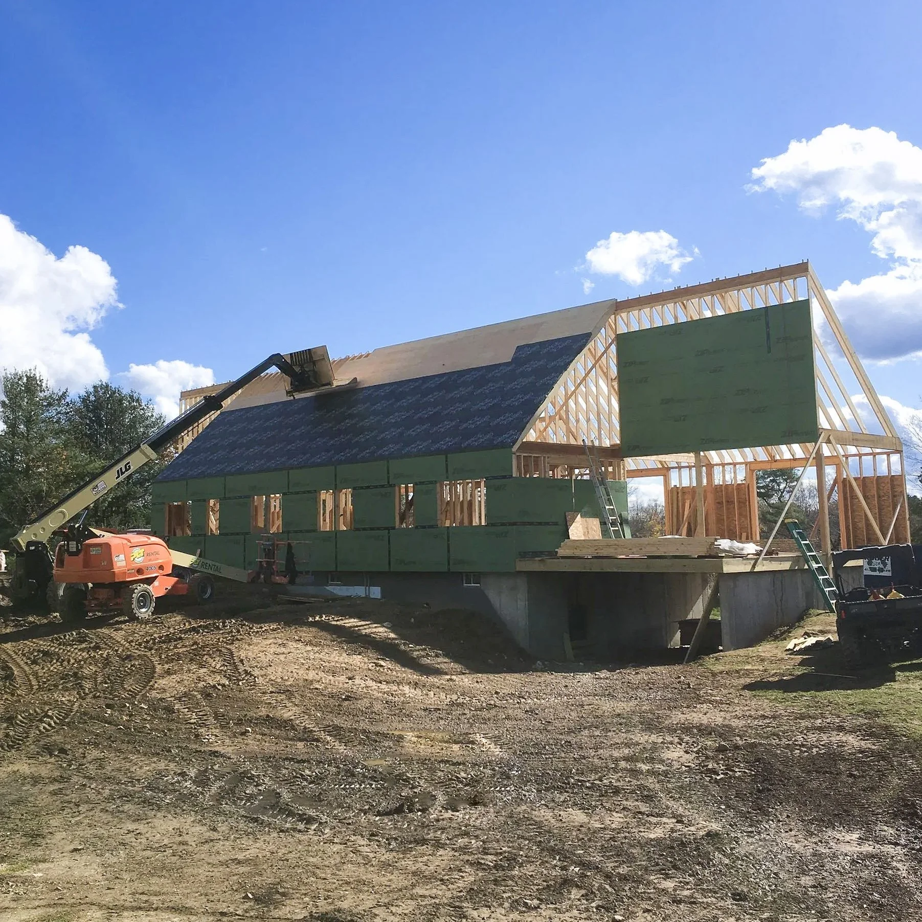 Construction site with a large residential home being built. A lift is on the left side of the home, indicating roof work