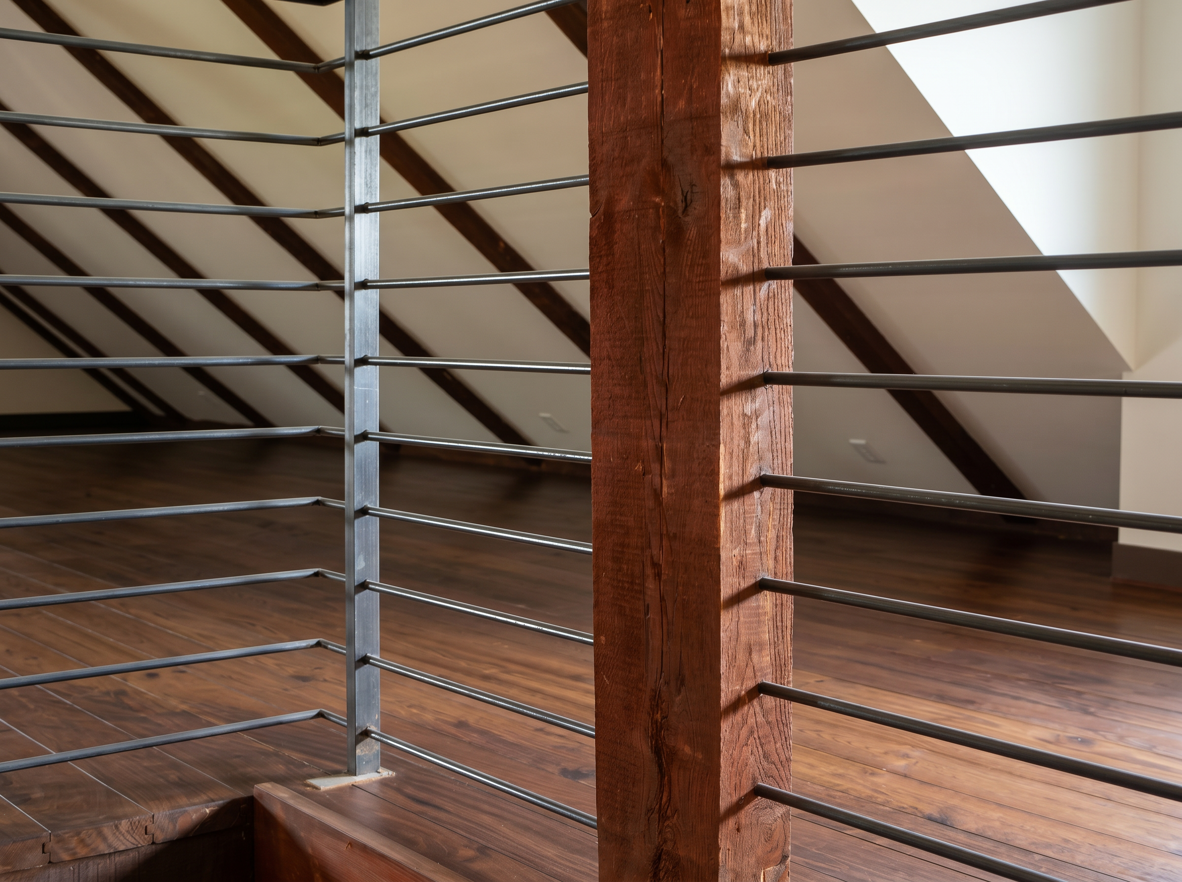 Close-up of a staircase railing with metal bars and a wooden newel post, set against a wooden floor and ceiling.