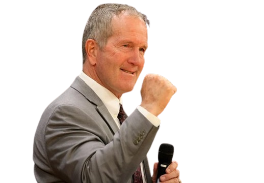 A man in a gray suit holding a microphone, smiling with his fist raised in celebration or triumph.